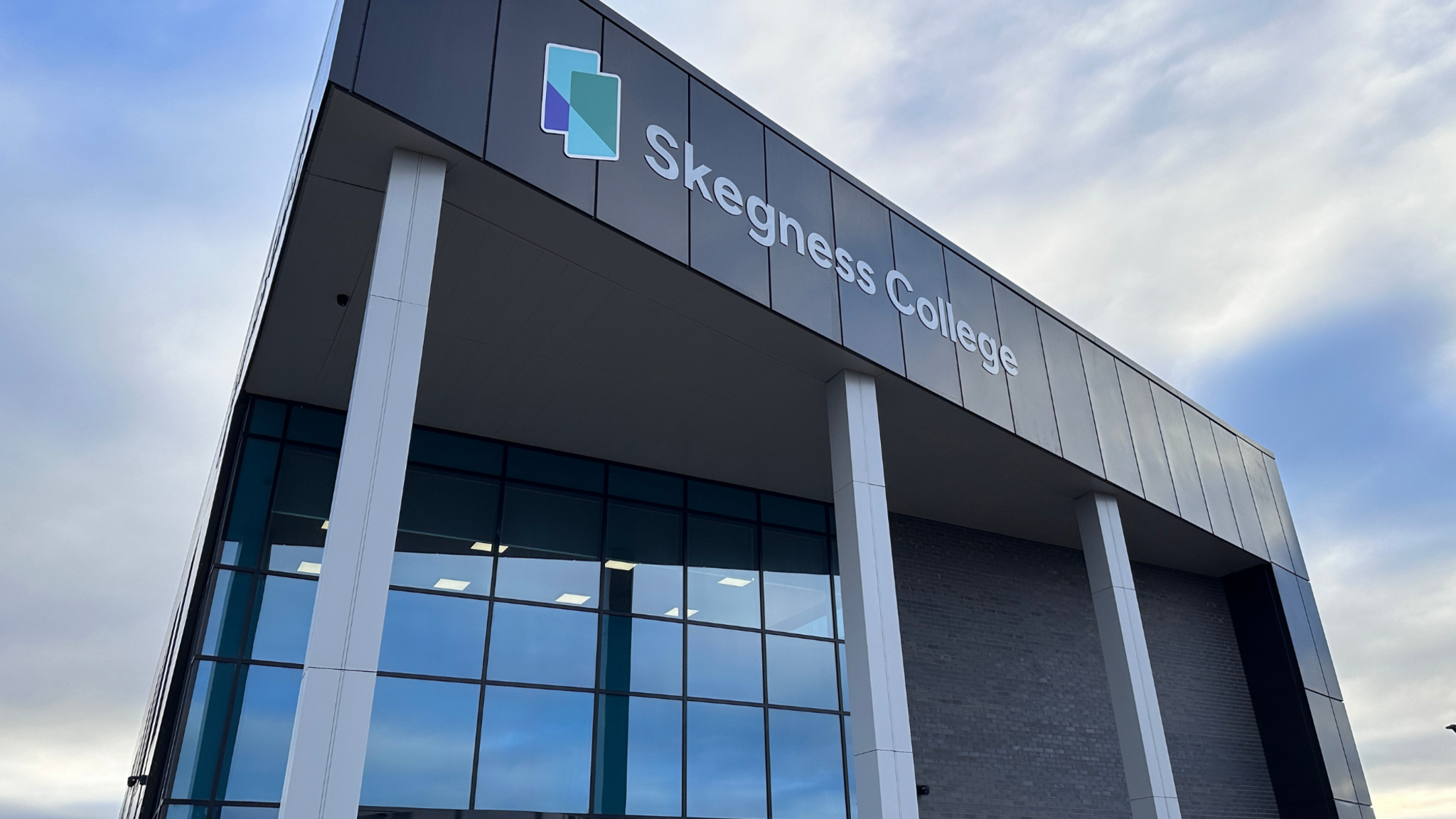 A building with glass windows. A sign says Skegness College.