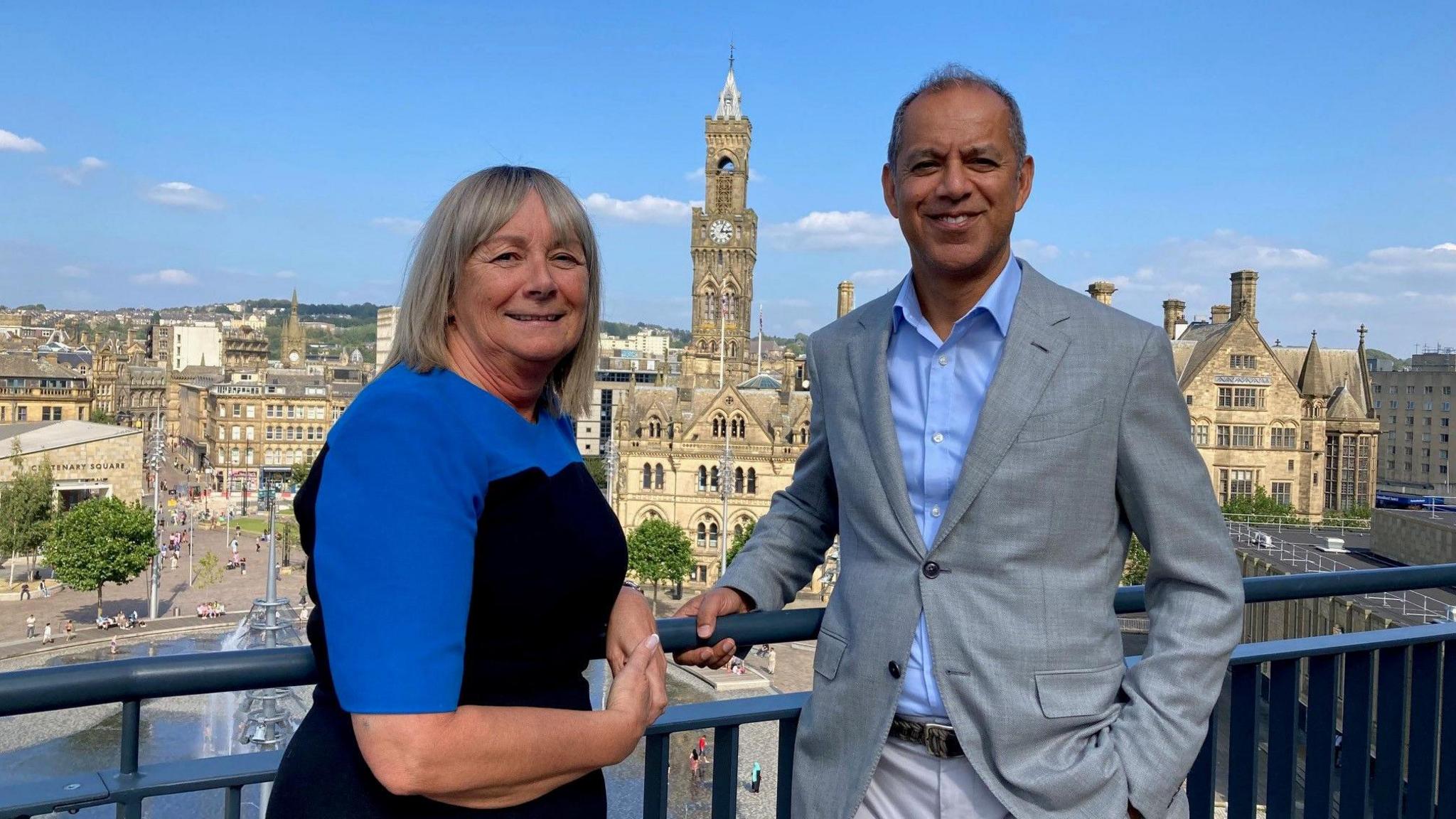 Jayne Child and Armoghan Mohamed from PwC on the balcony of their new  offices with Bradford's City Hall clock tower in the background