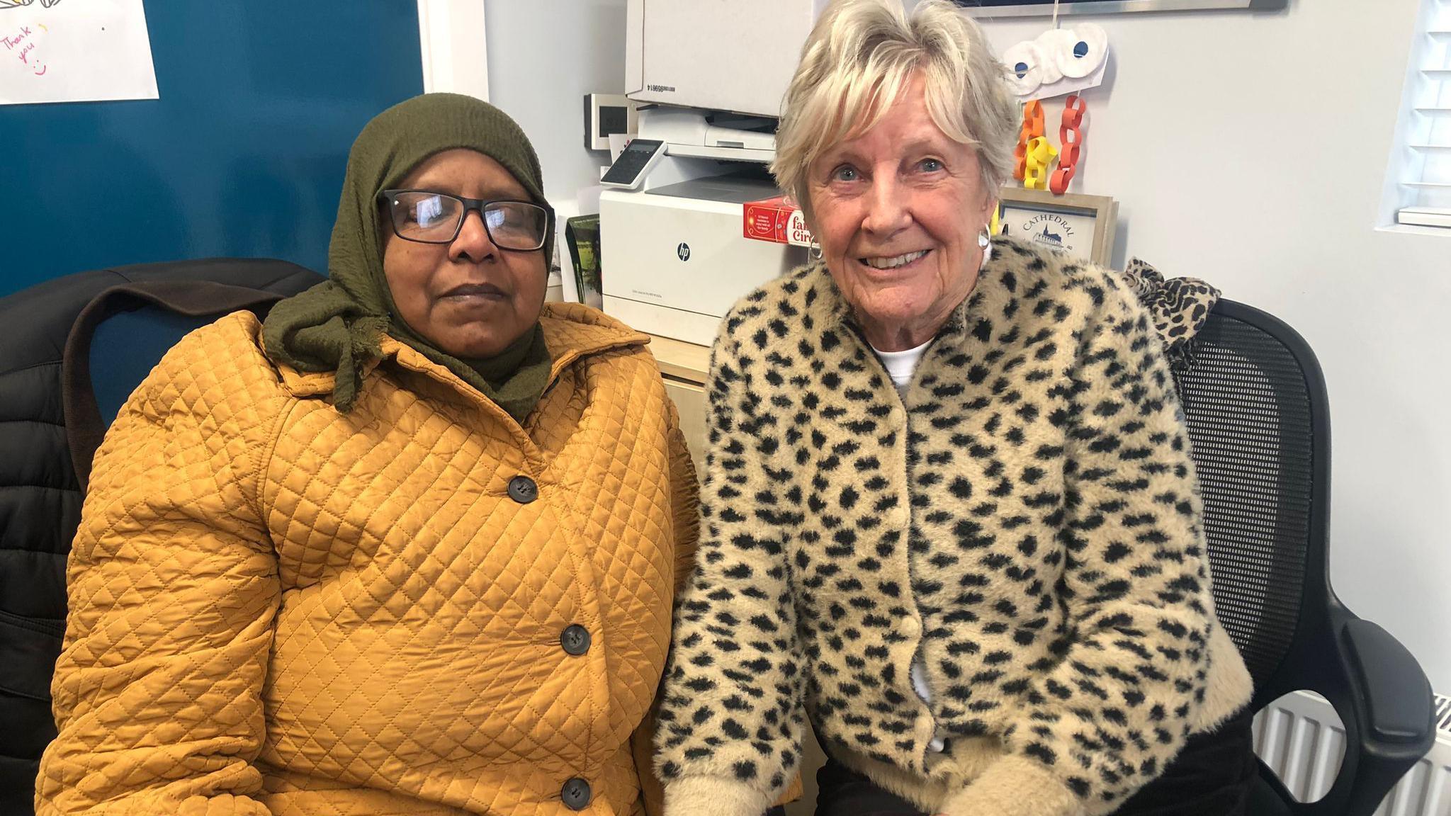 Hala Ahmed is on the left of the image wearing a head scarf, yellow caot and glasses. To her right is Jeanette Warke wearing a yellow coat on which there are blackspots. She has blonde hair. Both ladies are sitting side by side.