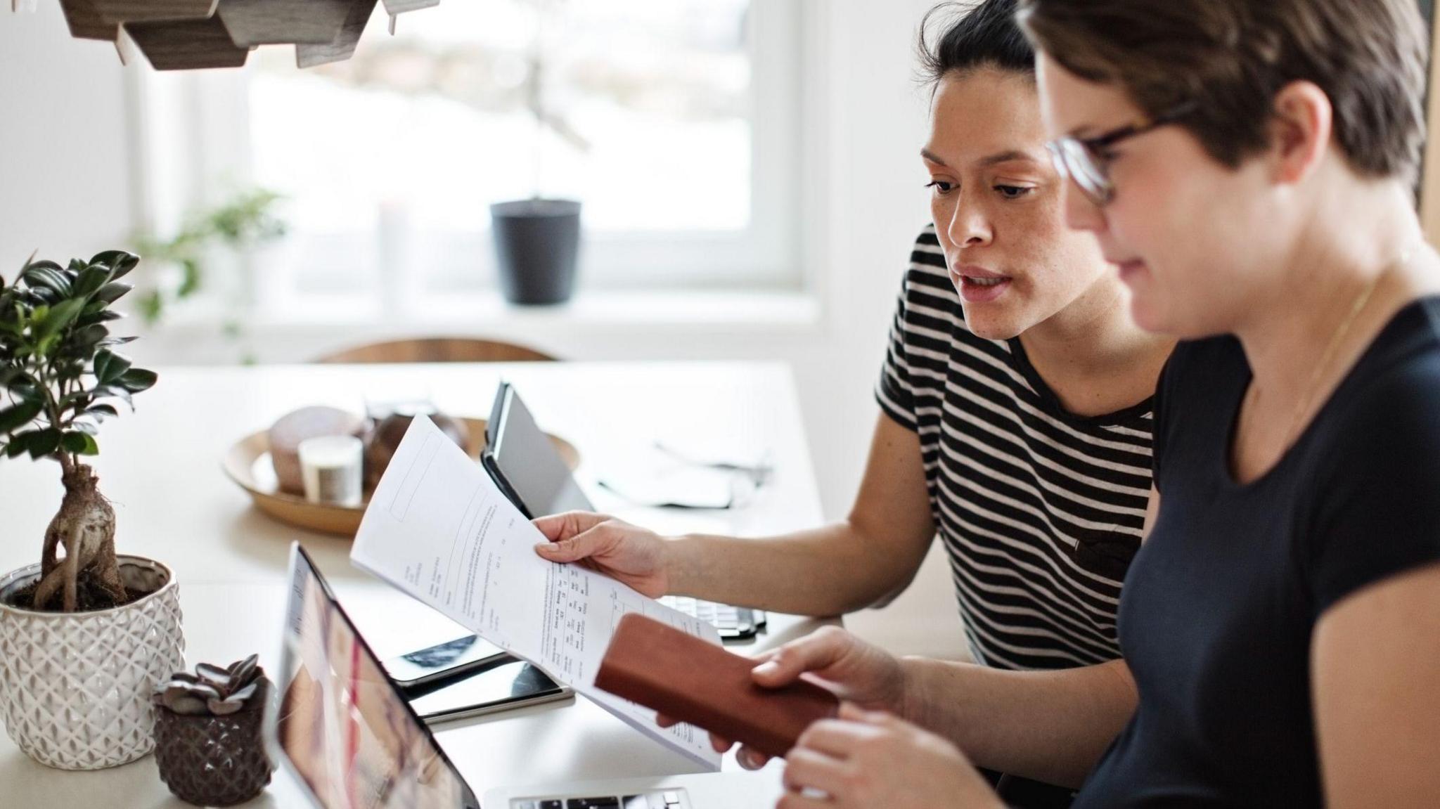 Two women look at a bill while sitting at a desk.