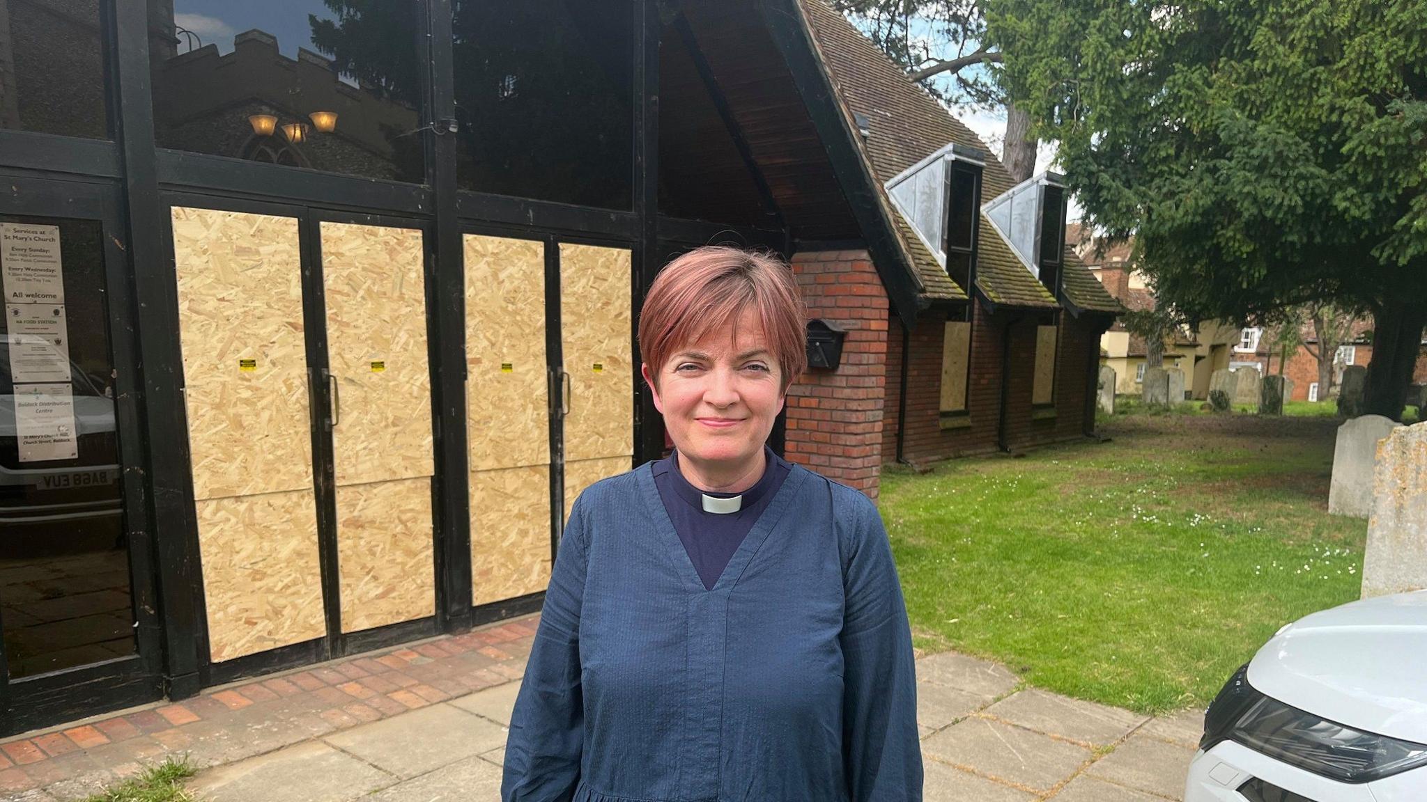 Church minister in dog collar outside boarded up church doors