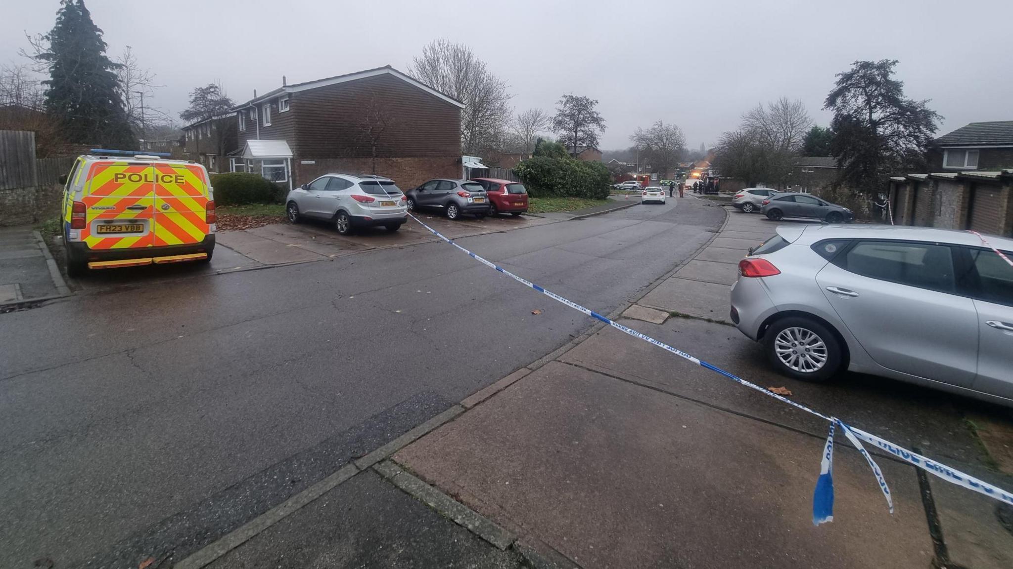 A police tape stretches across a road in a housing estate. 