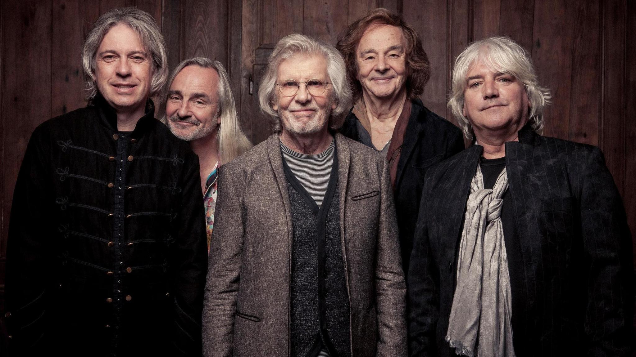 The Zombies band in a recent photo. Rod Argent is centre wearing glasses and a speckled suit jacket and striped T-shirt, he is smiling at the camera and has grey medium-length hair and stubble. 