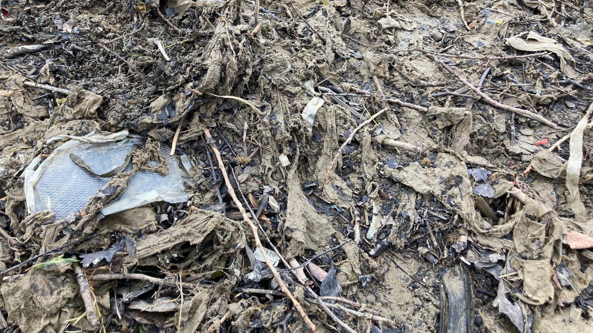 A close up image of sludgy brown wet wipes congealed together with mud and other litter from the river.