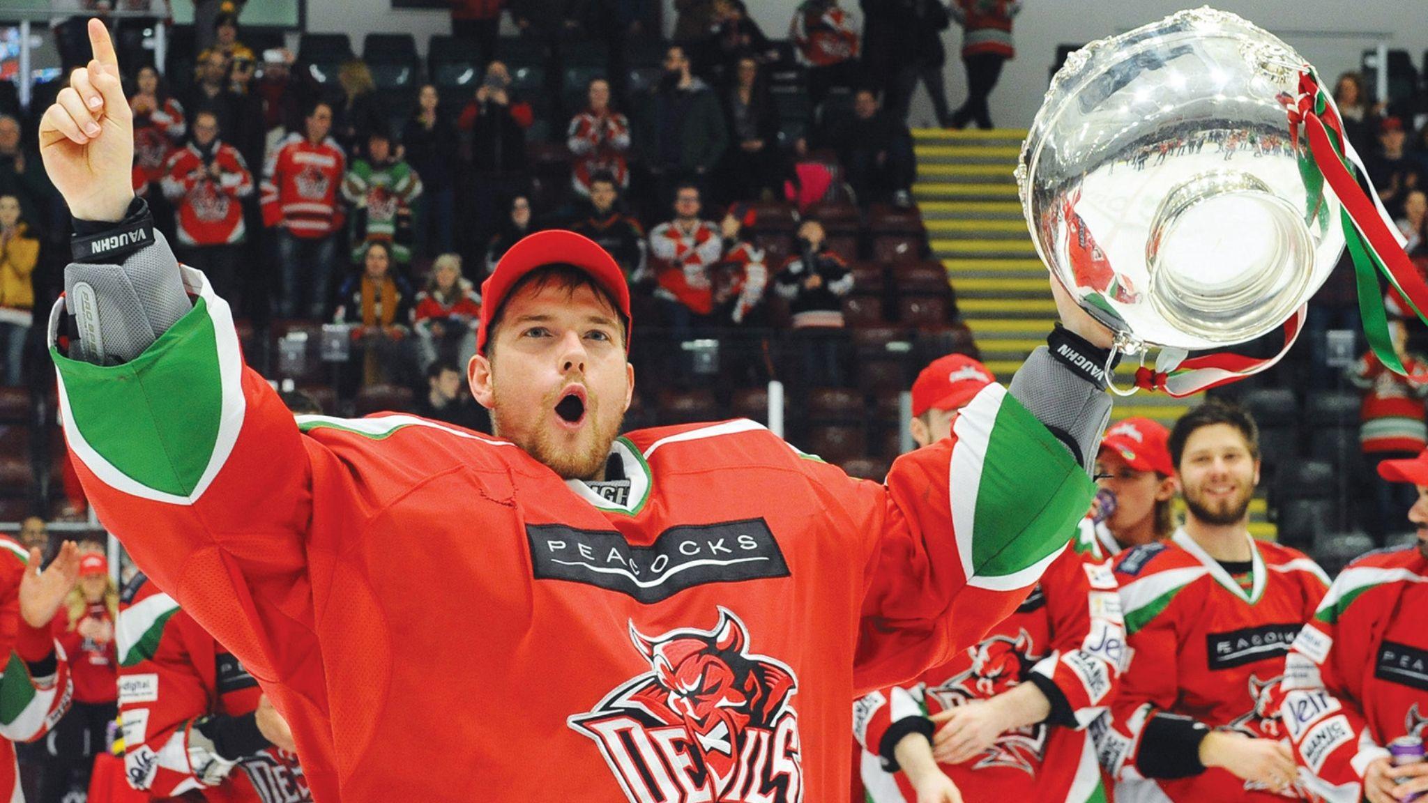 Ben Bowns in red jersey and cap holds arms aloft with trophy in left hand