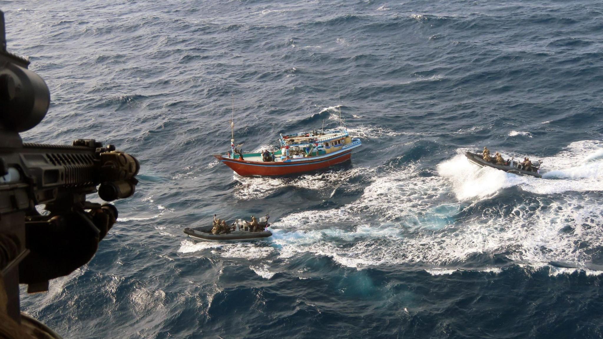 The barrel of a sniper looking down on two Royal Marine ribs closing in on a small sailing boat.