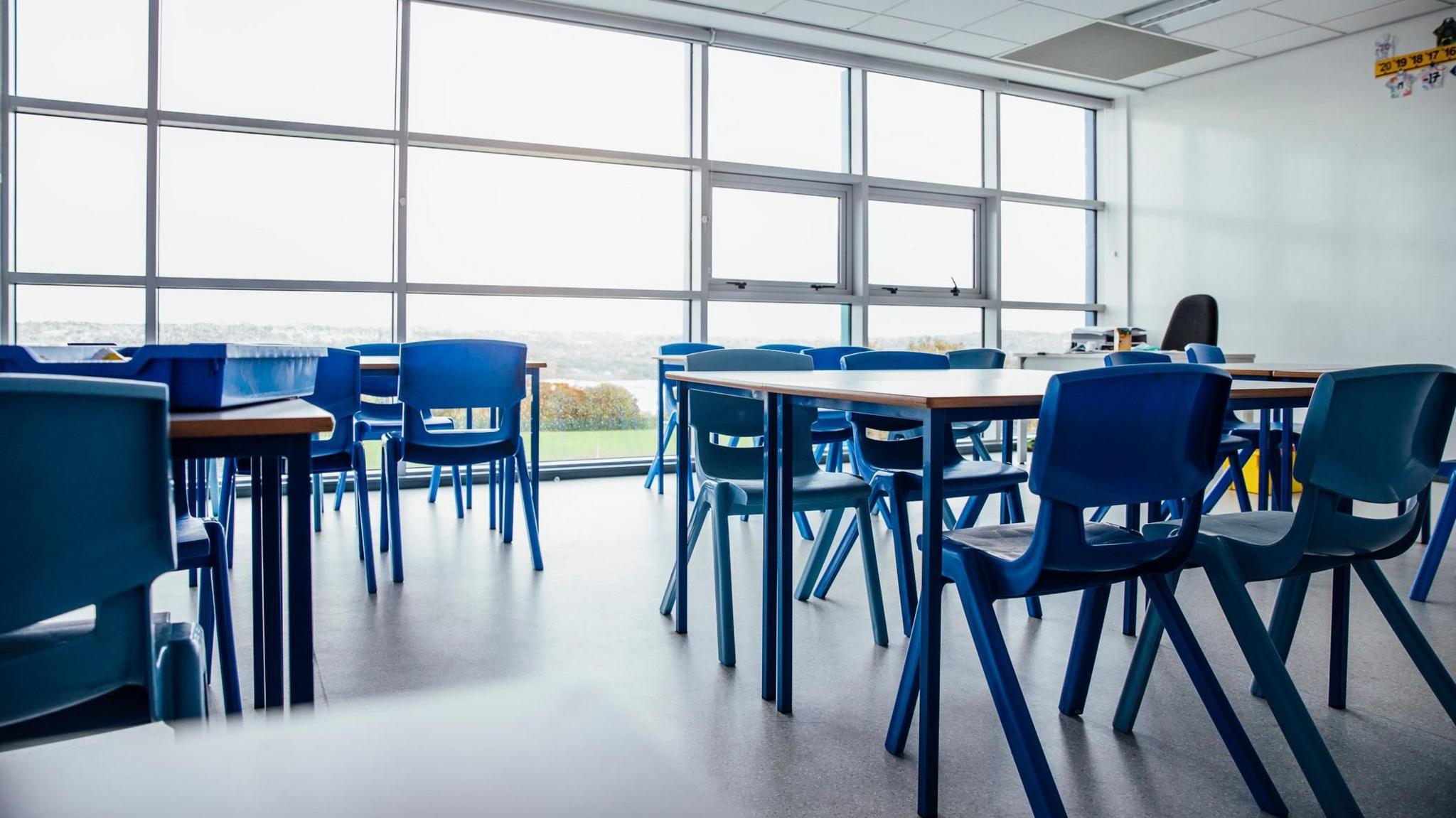 A classroom with tables and chairs but no pupils