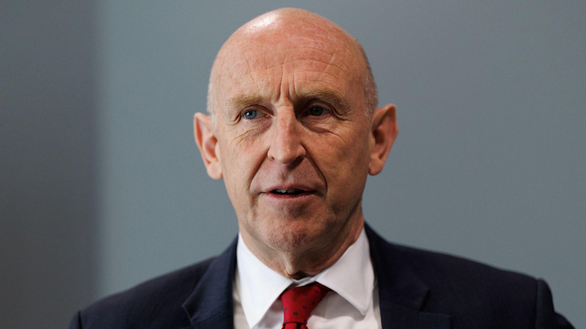 A bald headed man in a dark suit with a red tie and white shirt