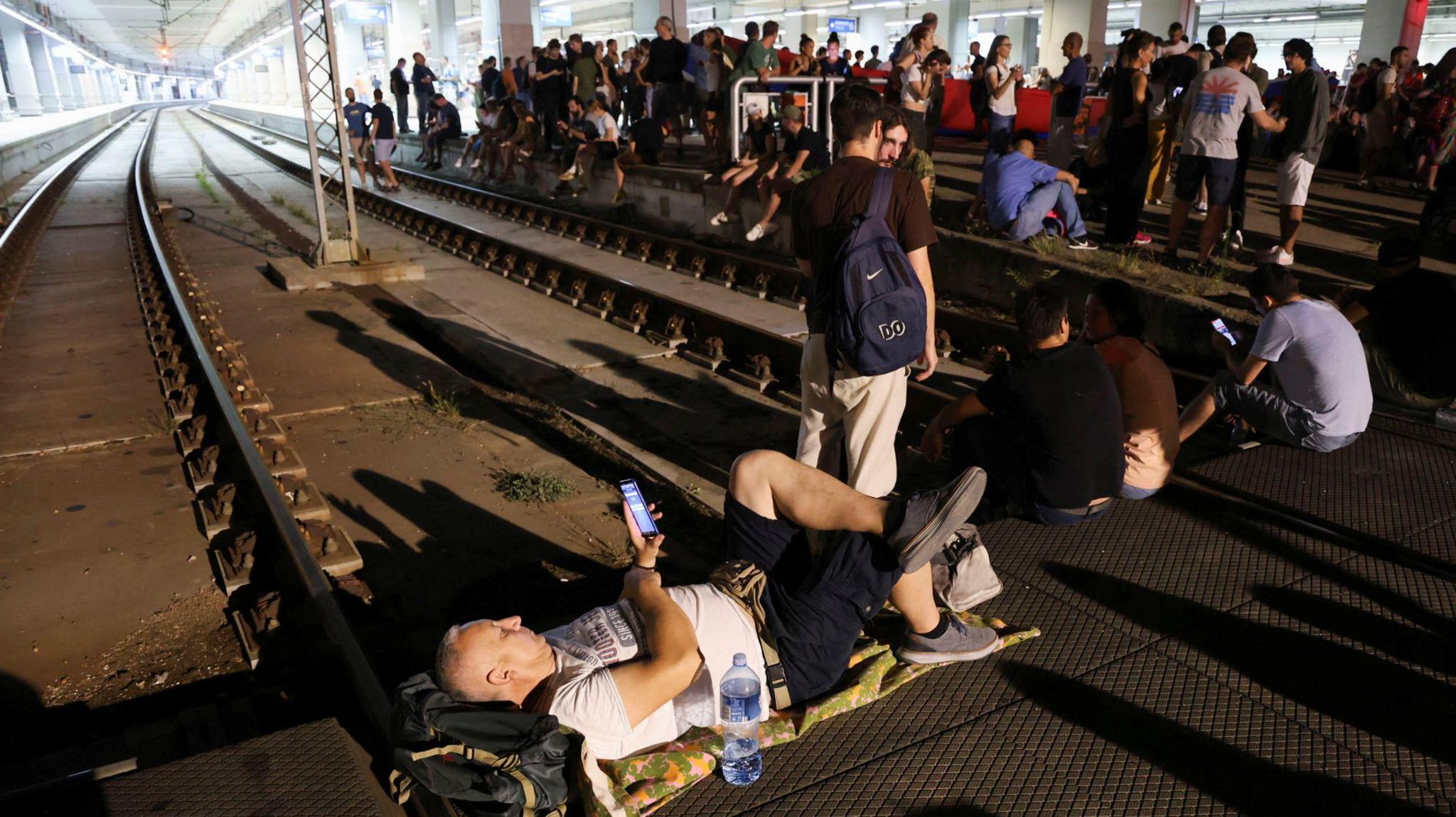 A person lying on train tracks and several others standing on the track and near it