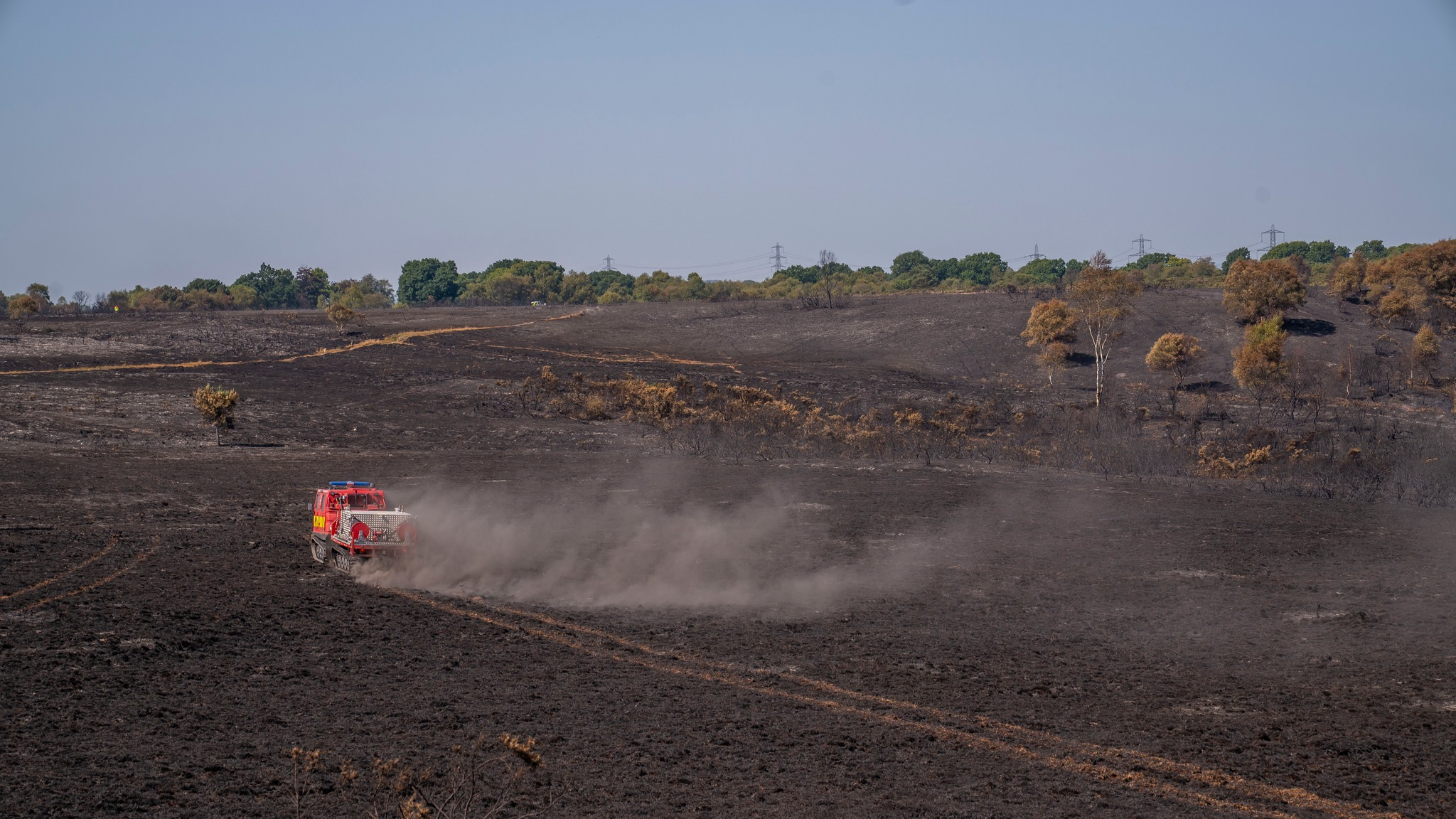 A picture that shows large areas of damage after the fire and a fire service vehicle driving across the scorched land.