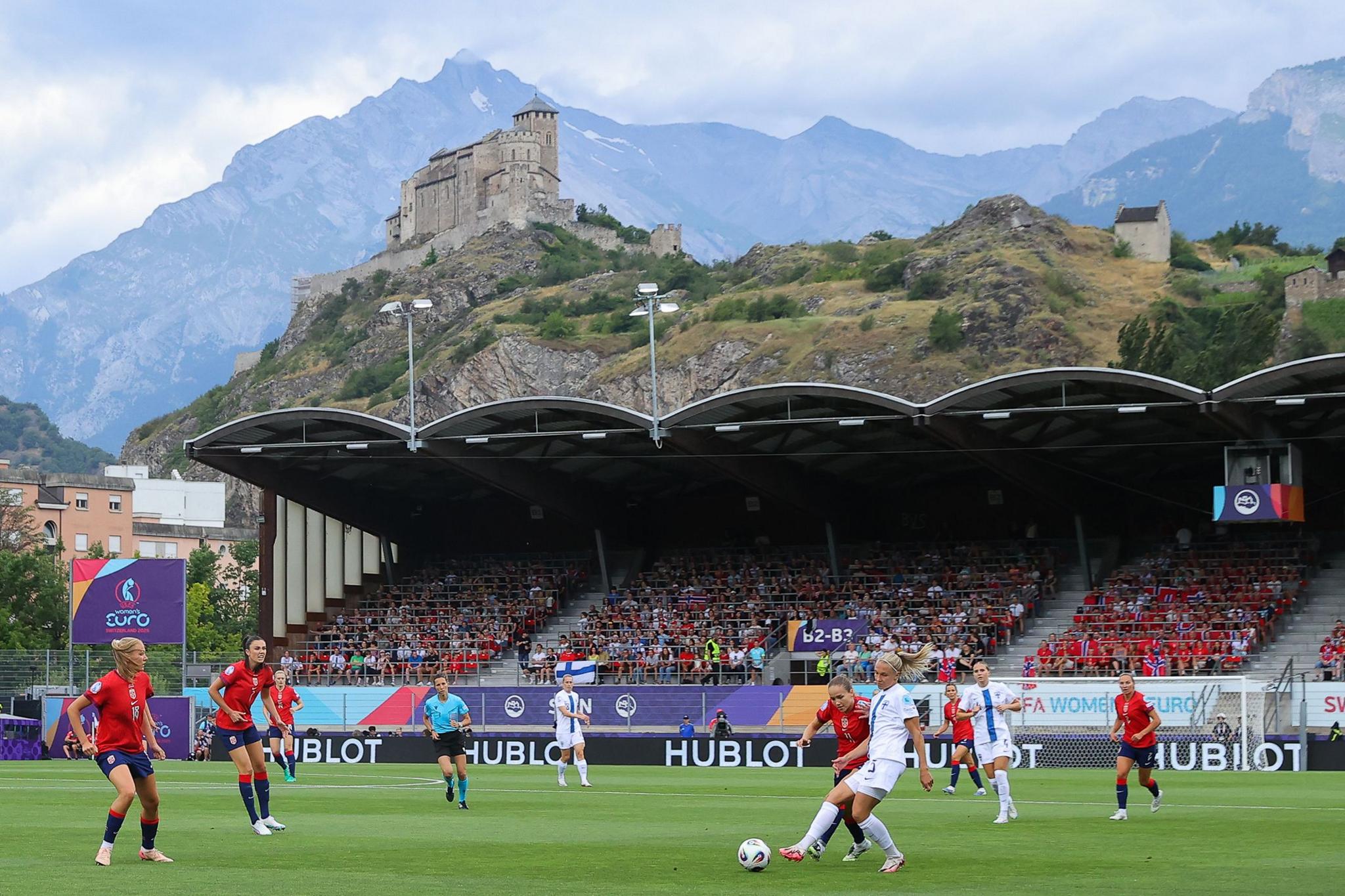 Match action is seen overlooked by distant mountain Haut de Cry and nearby landmark Basilique de Valere during the match at Stade de Tourbillon. Photo by James Gill