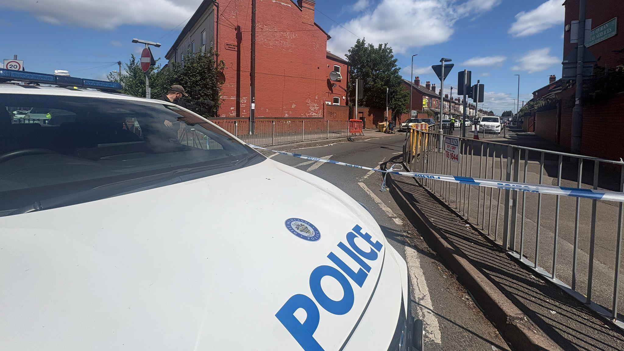 A West Midlands police vehicle at the scene. It is in front of the blue and white police tape. 