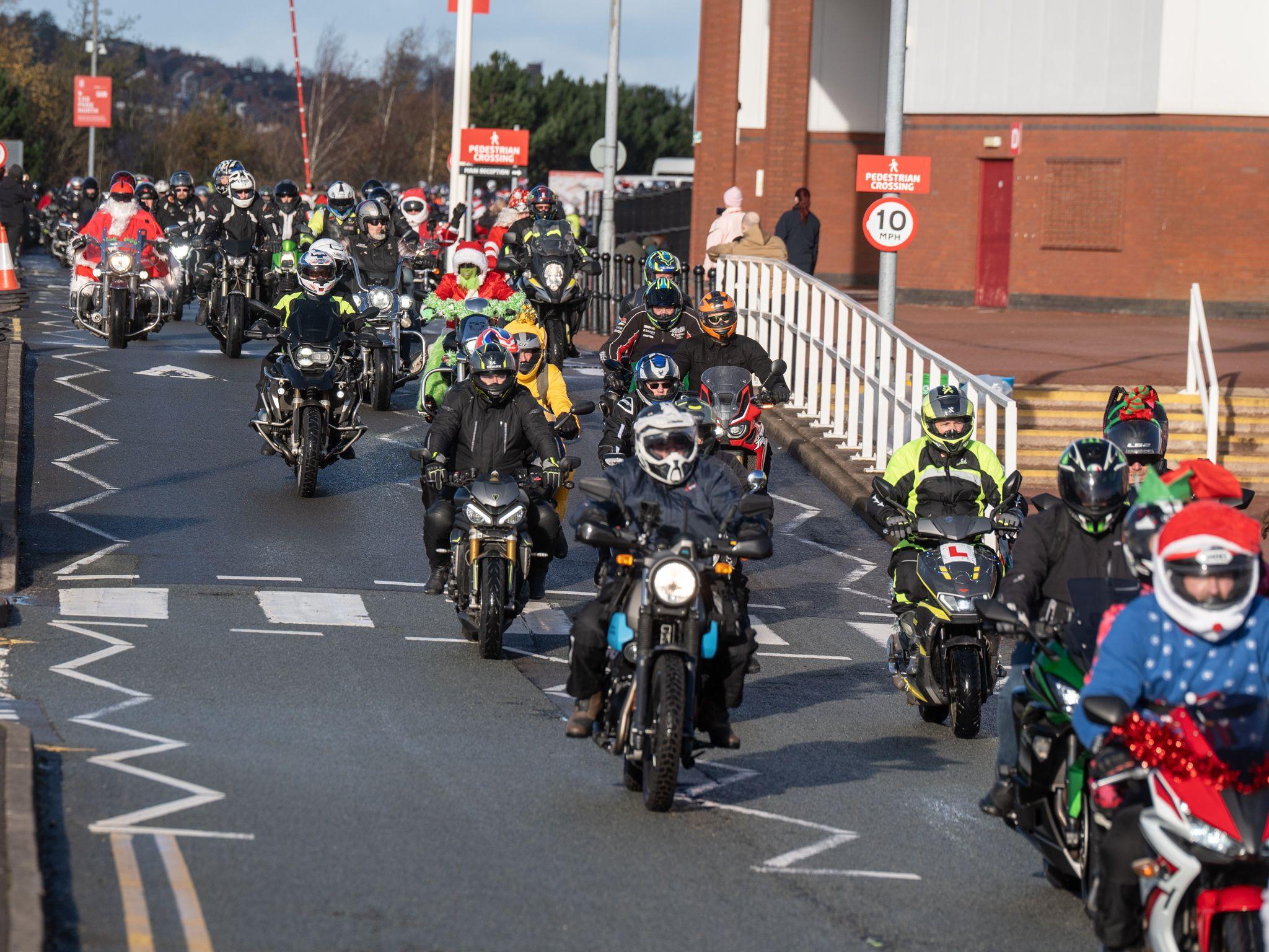 A group of bikers set off on a charity motorcycle ride from the Bet365 Stadium car park. There are double yellow lines and a pedestrian crossing and other street furniture in the image.