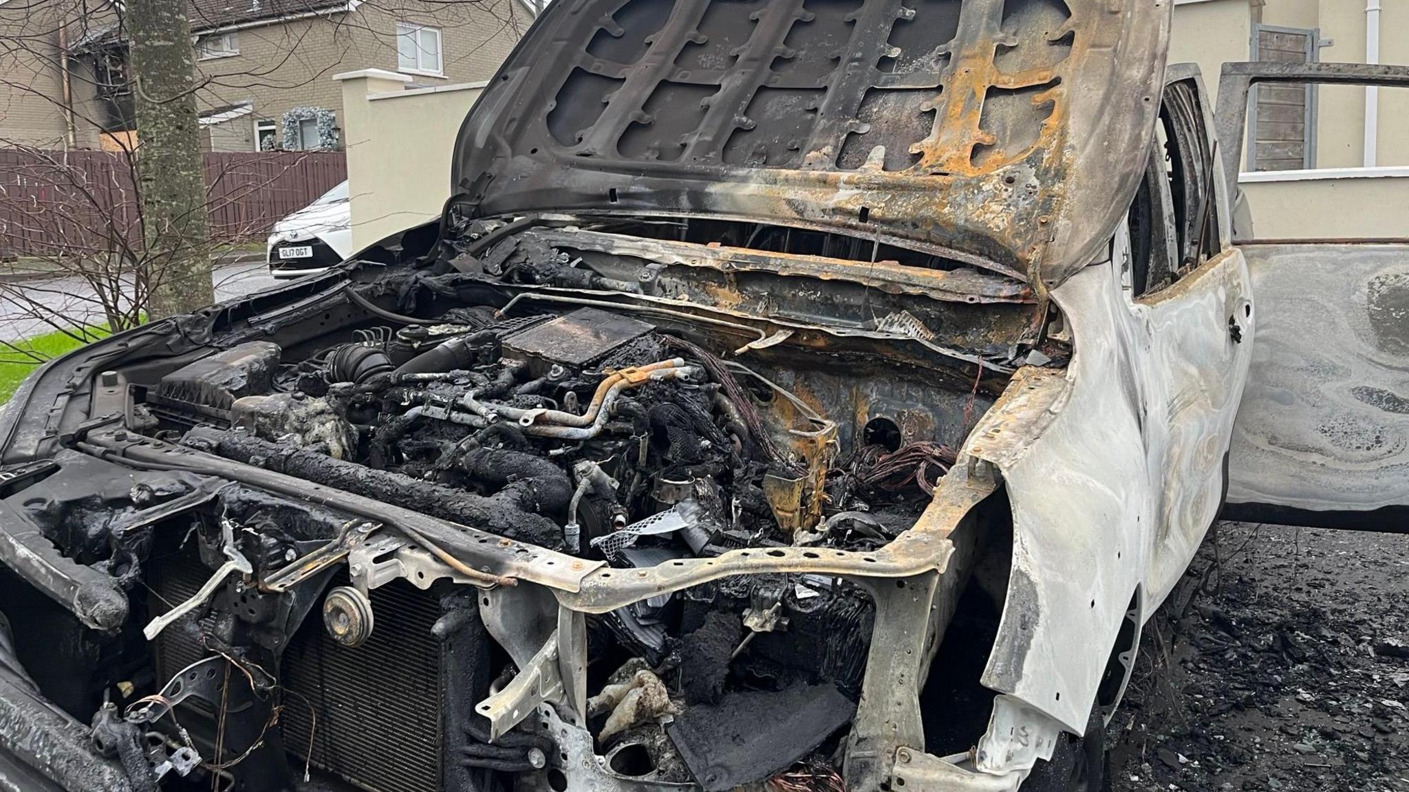 A burnt-out car, the bonnet is up and one door is open