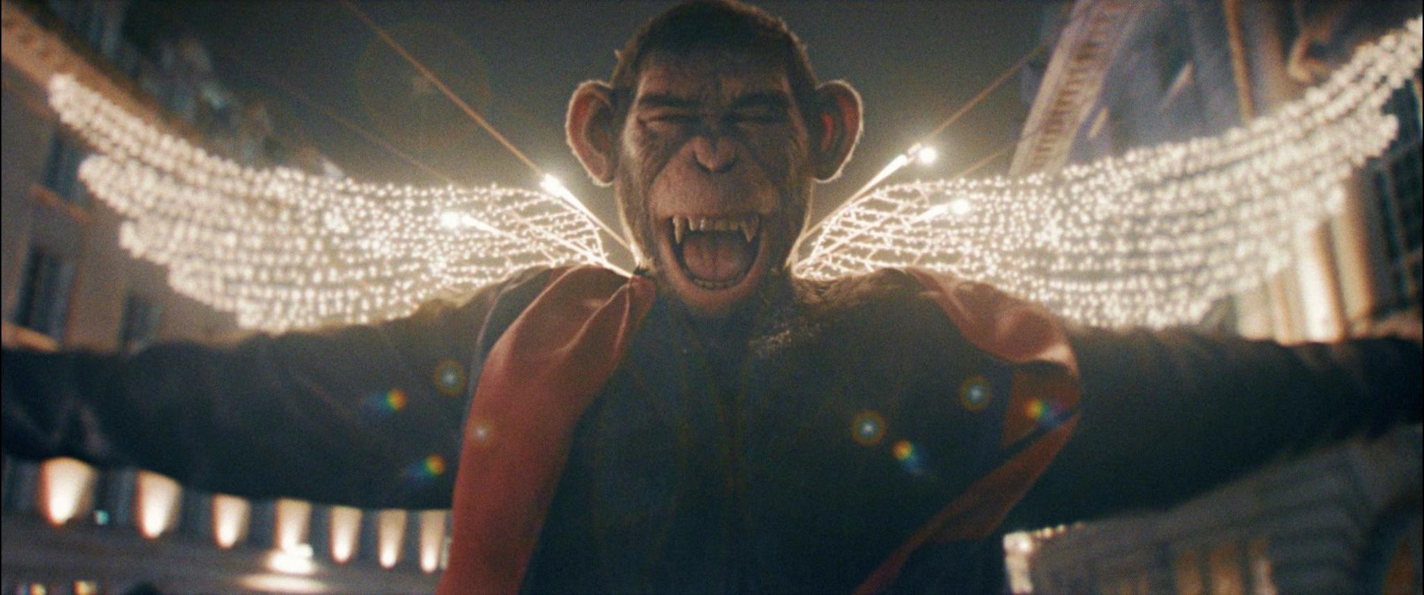 A still from the film shows the chimpanzee character with its arms outstreched and its mouth open, outside on a street with angel wings made of lights in the background.