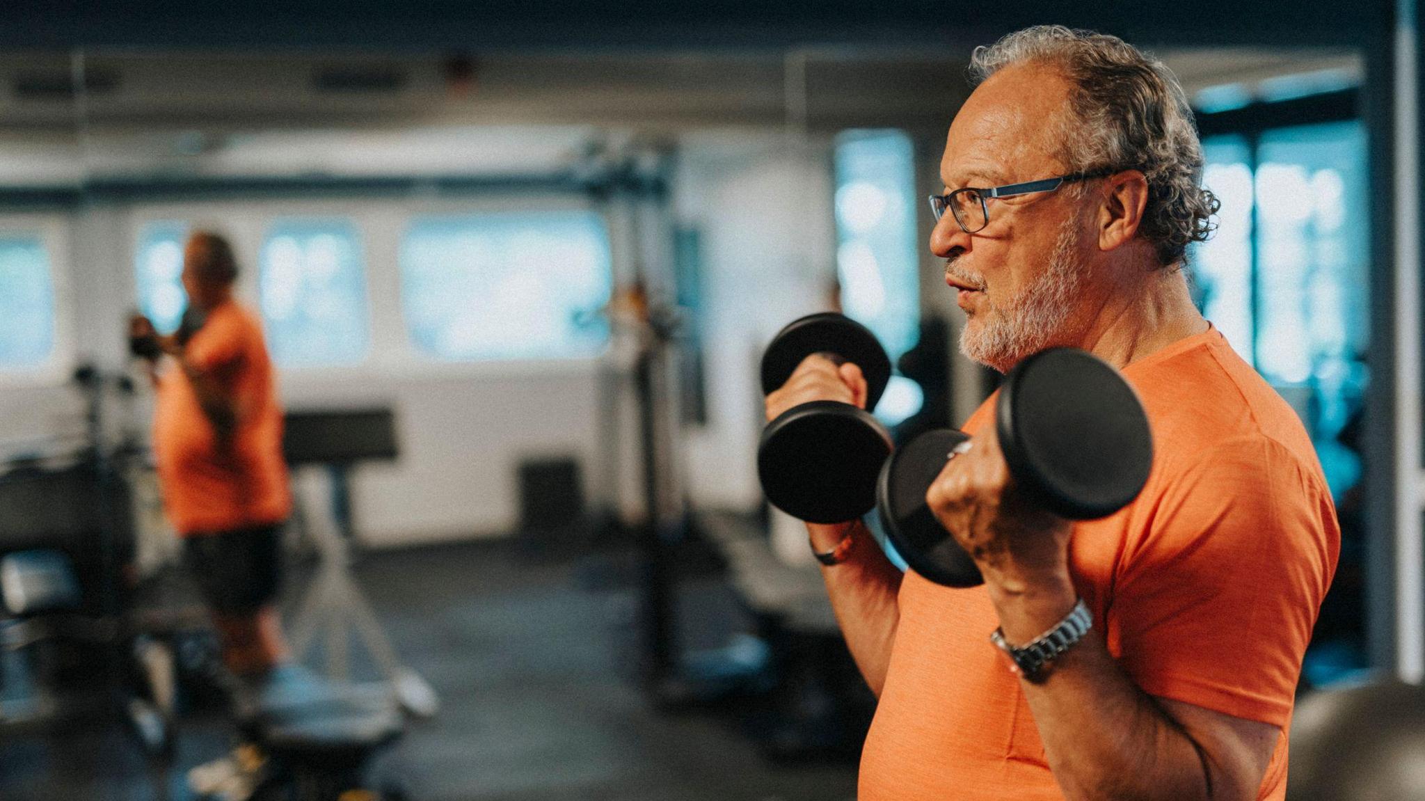 Side view of active senior man with dumbbells exercising at health club - stock photo