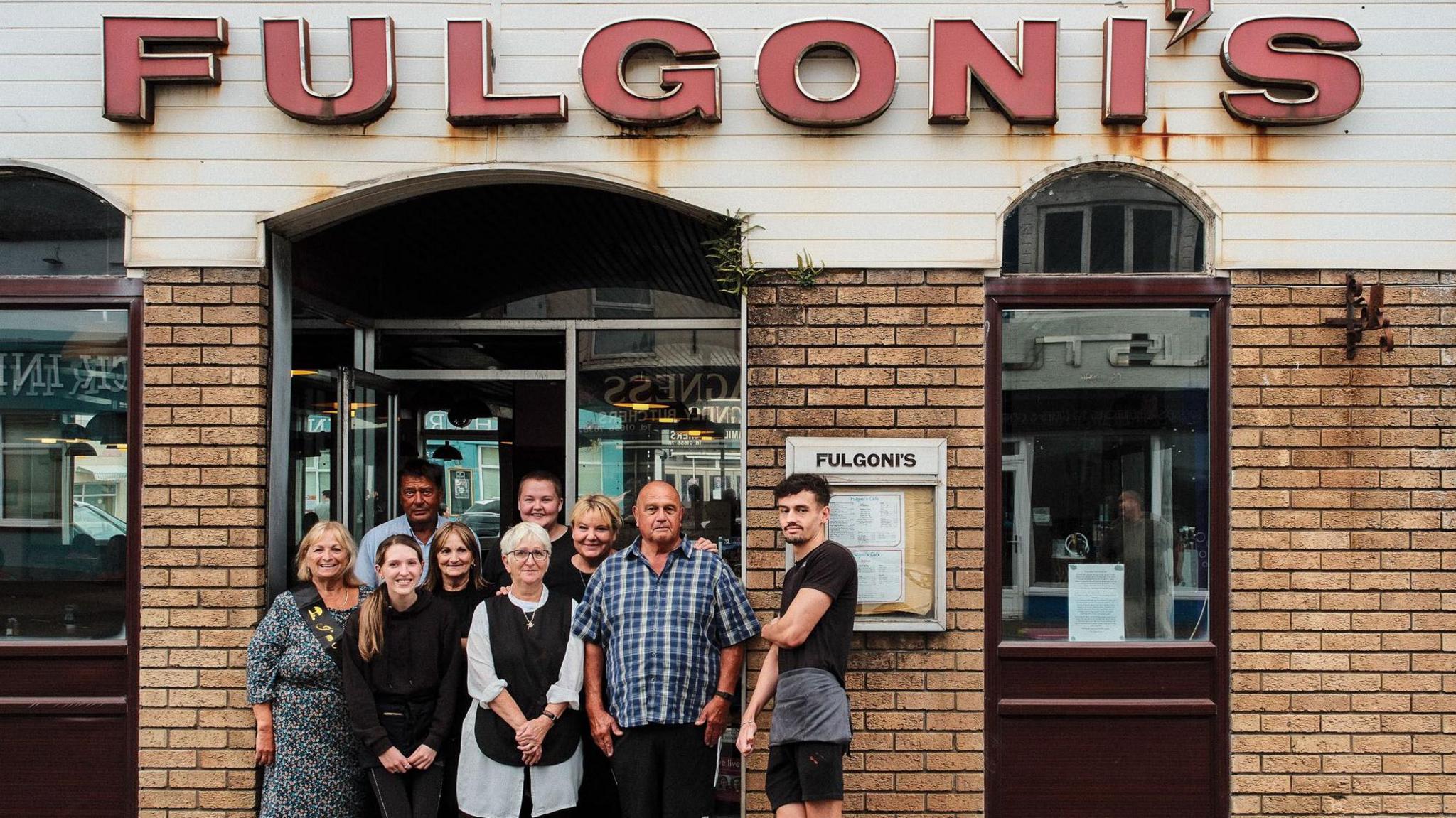 The Fulgoni family, nine people of multi-generations stand in the entrance of their cafe