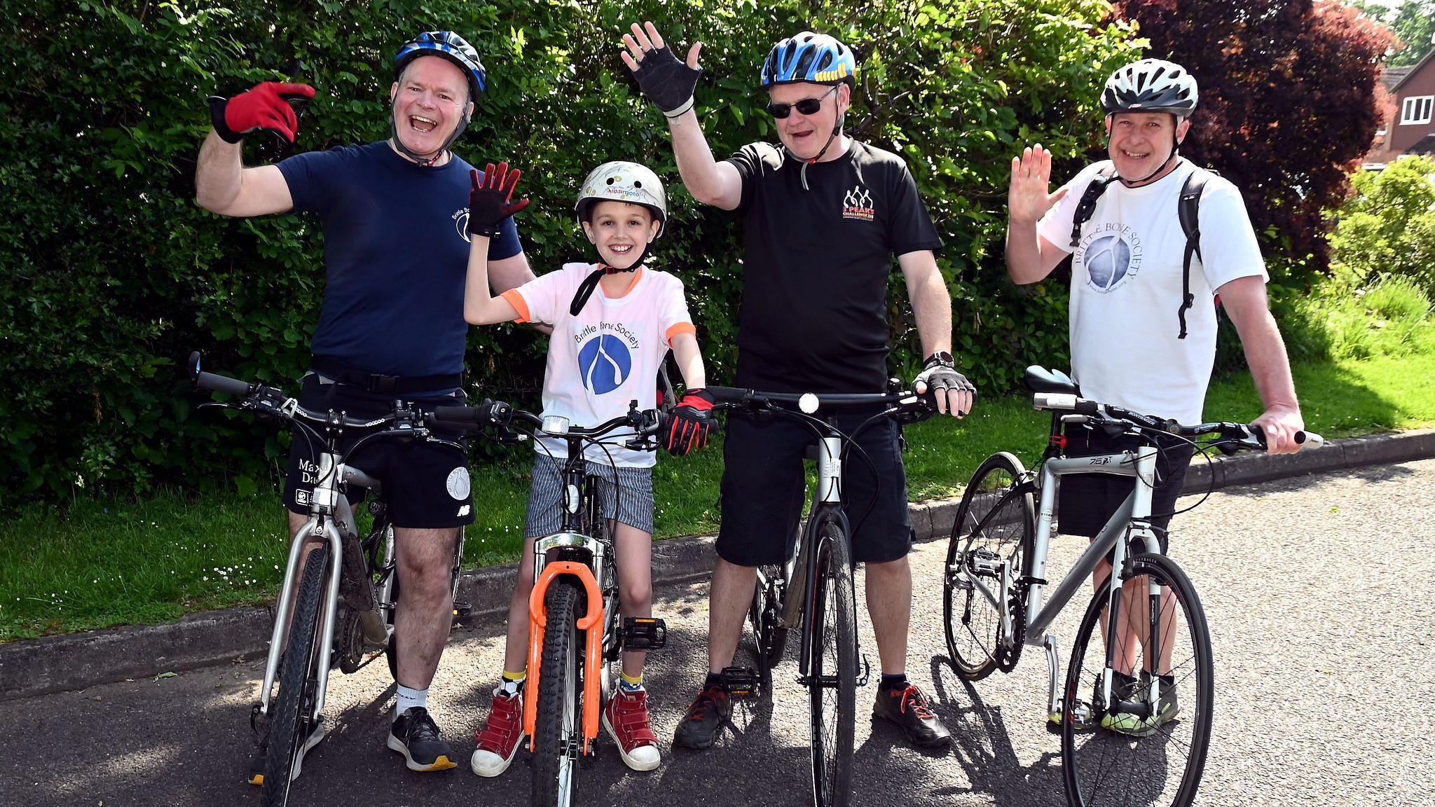 Steve and Max on their bikes, along with two other cyclists, both men. They are all waving at the camera