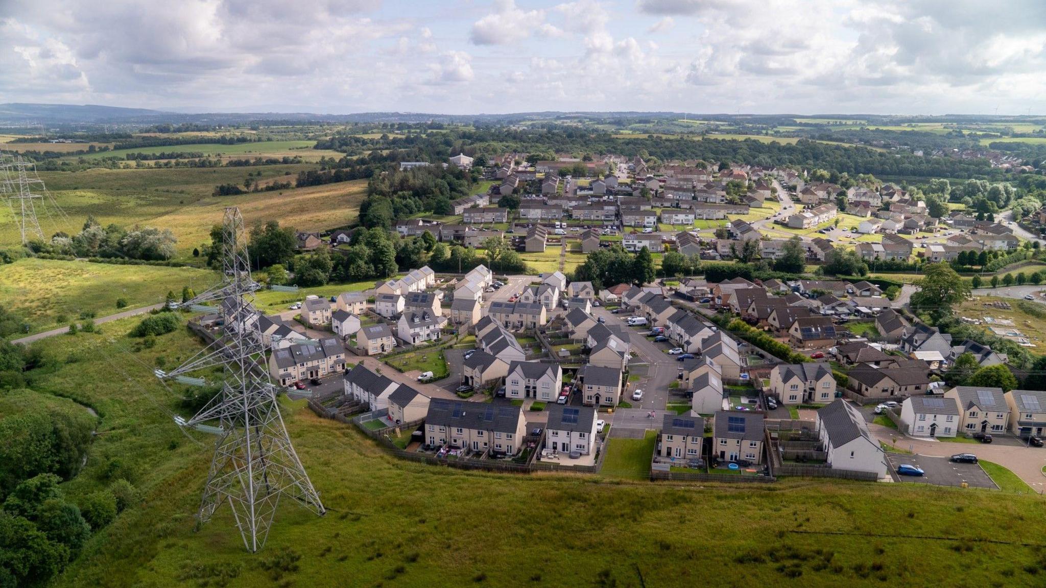 An aerial image of a new housing scheme with electricity pylons passing one side of the properties