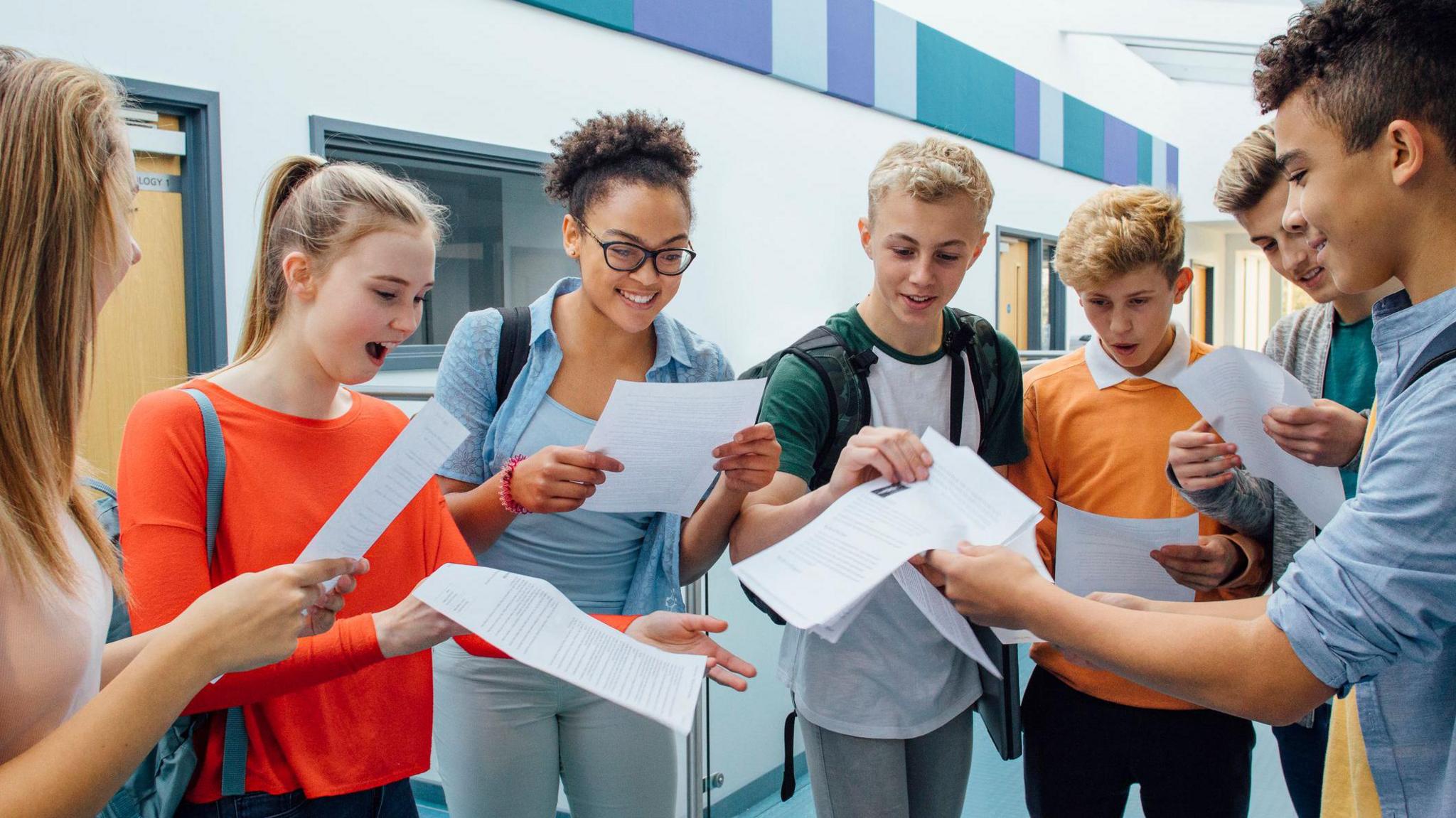 A group of teenagers gather round and open their exam results envelopes