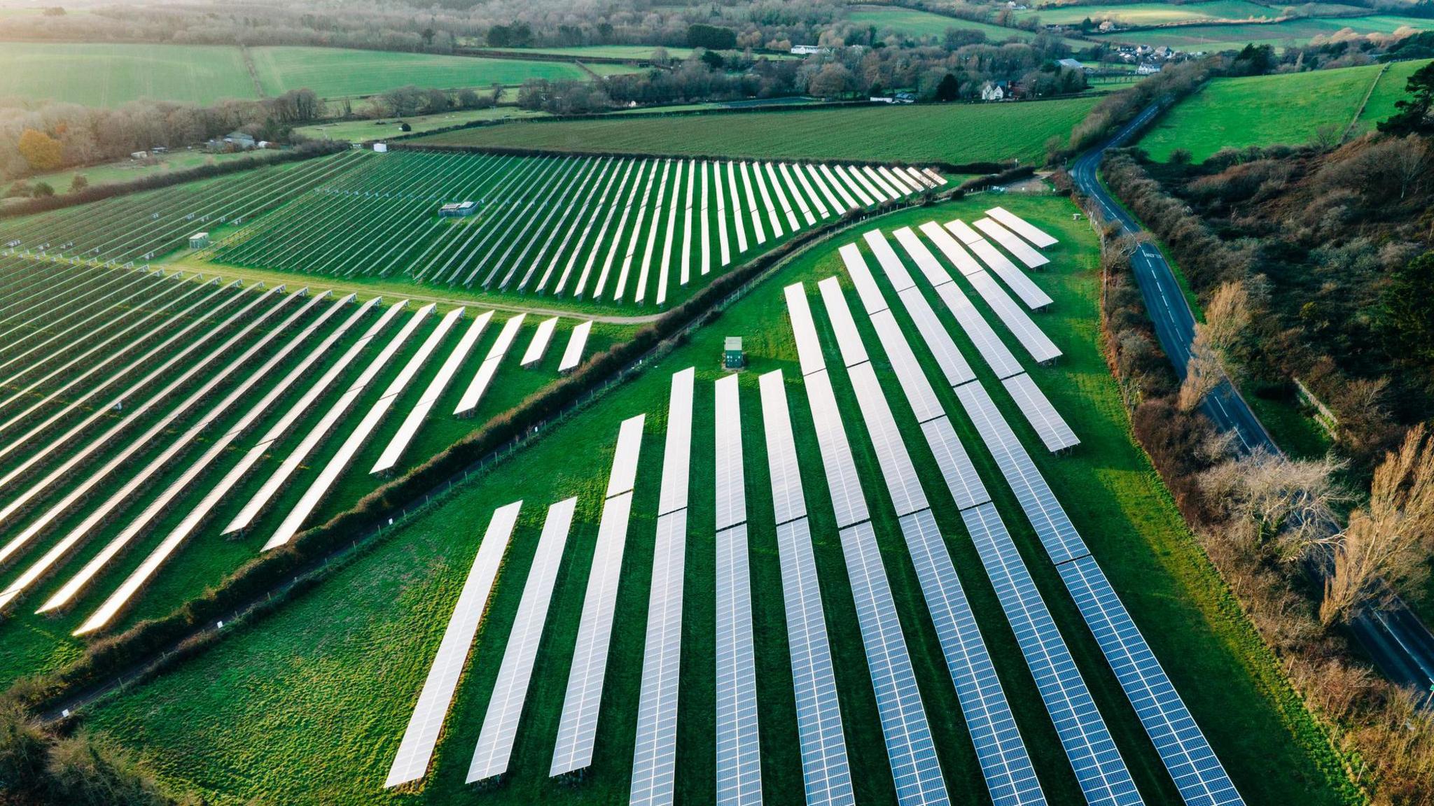 A stock picture of a solar farm. There are rows of solar panels in a field. 