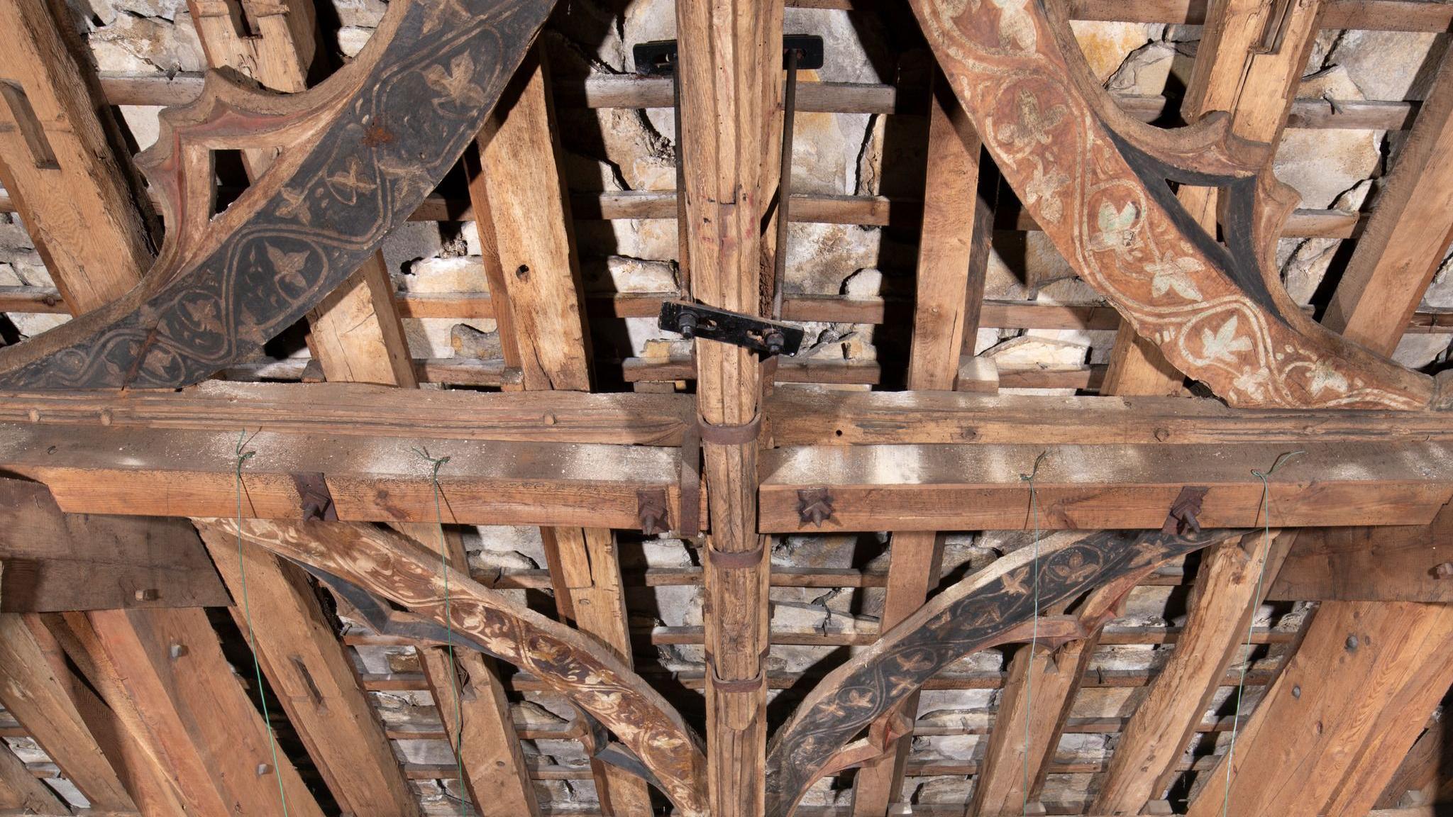 The medieval wooden beamed roof of Christchurch Priory. Large interconnected beams decorated with black and brown paintings, connected with smaller slats.