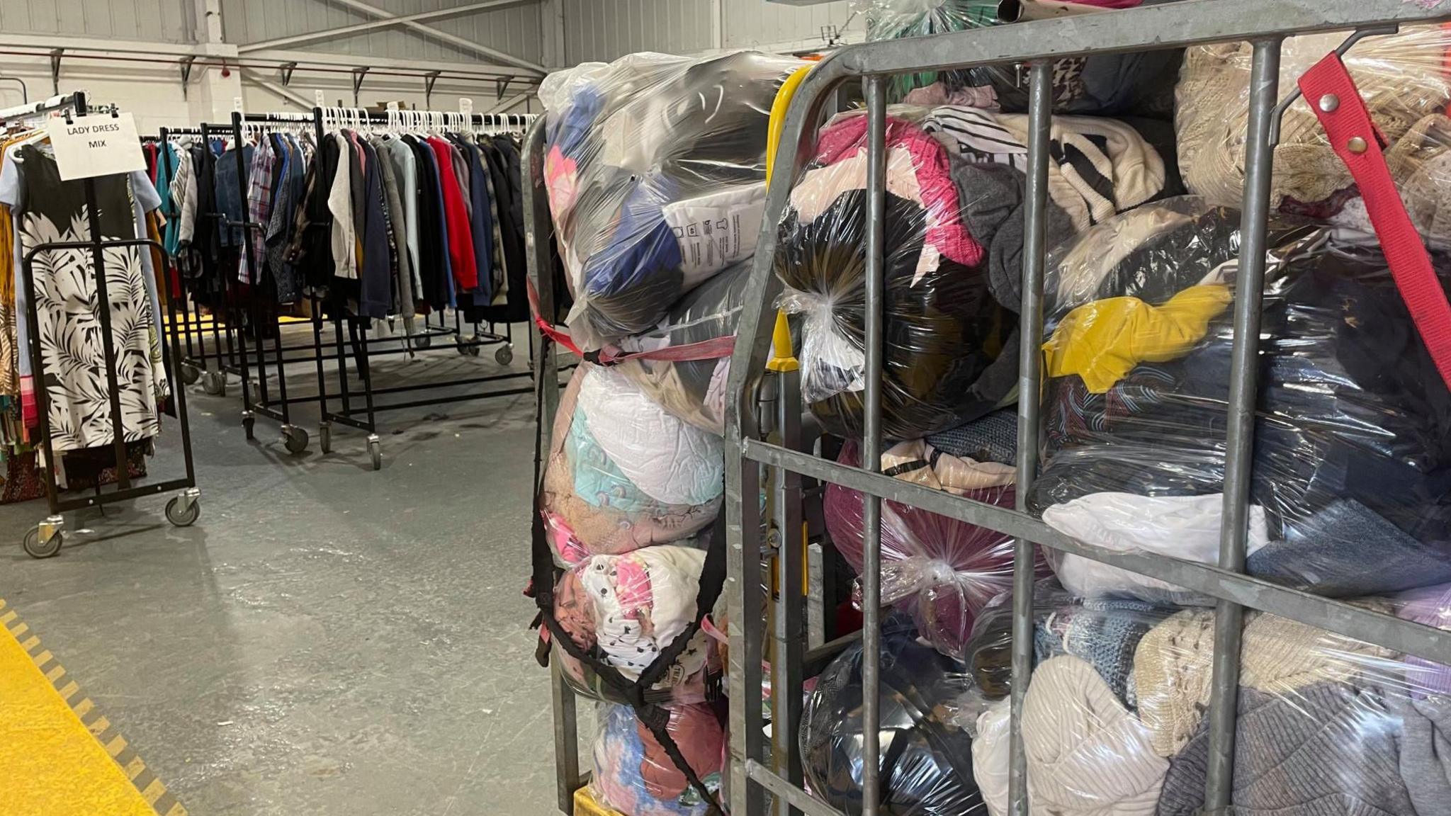 A large warehouse with rails of clothes and caged trollies of bagged materials
