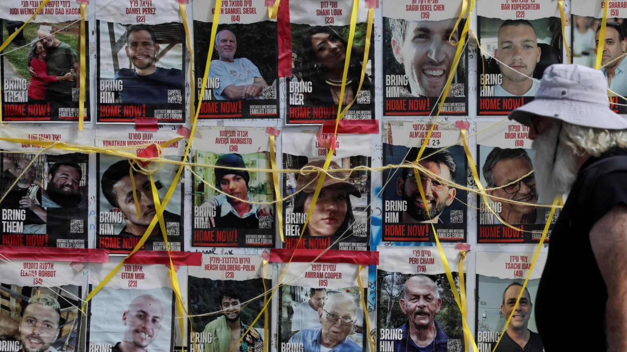 A man walks past a wall of posters in Tel Aviv, Israel, showing Israeli hostages being held by Hamas in Gaza (22 July 2024)