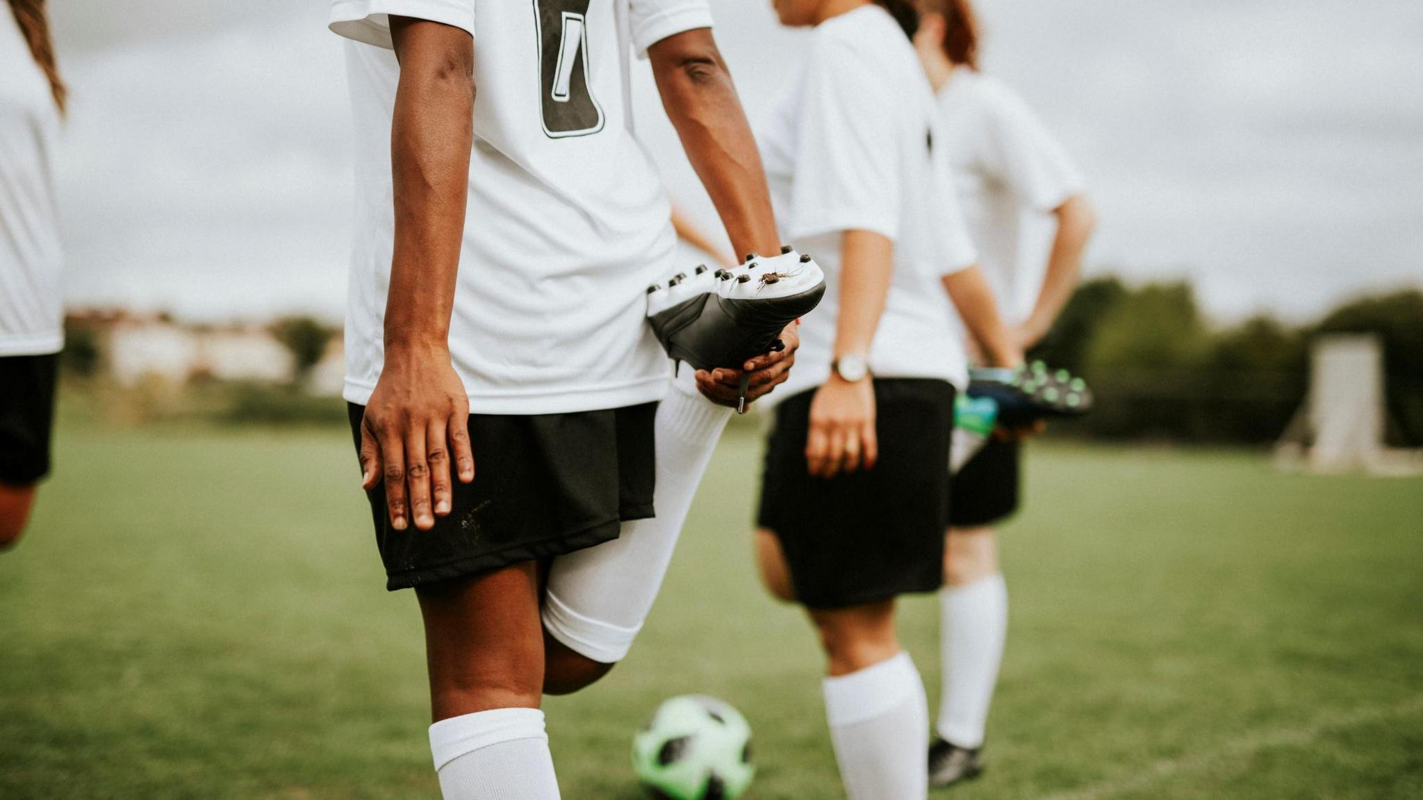 Female footballers wearing white shirts and black shorts with their backs to the camera