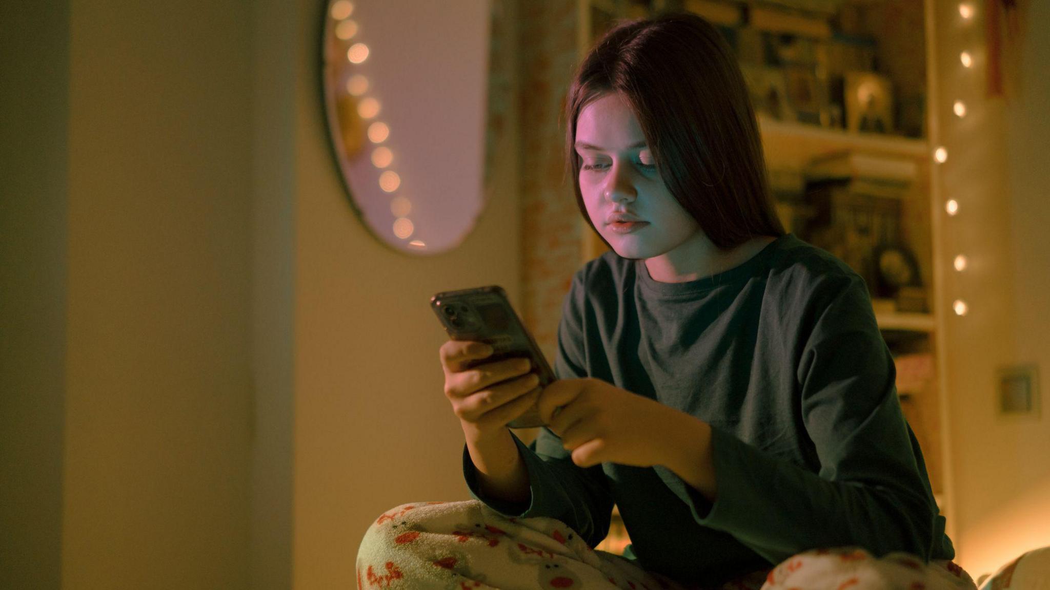 Teenage girl sits on a bed on her phone