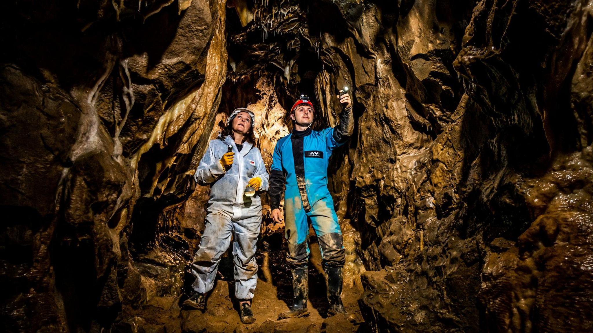 Lisa and Oliver Bowerman wearing mud-splattered caving over-suits, helmets and head torches in the new cave