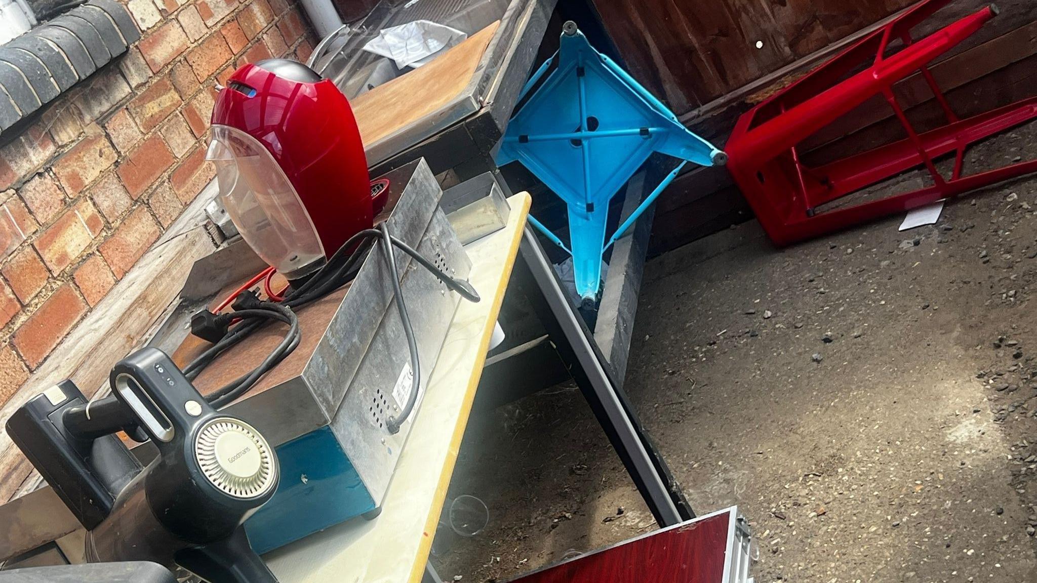 Two stools red and blue have been pushed to the ground and other garden equipment displaced around a table. 