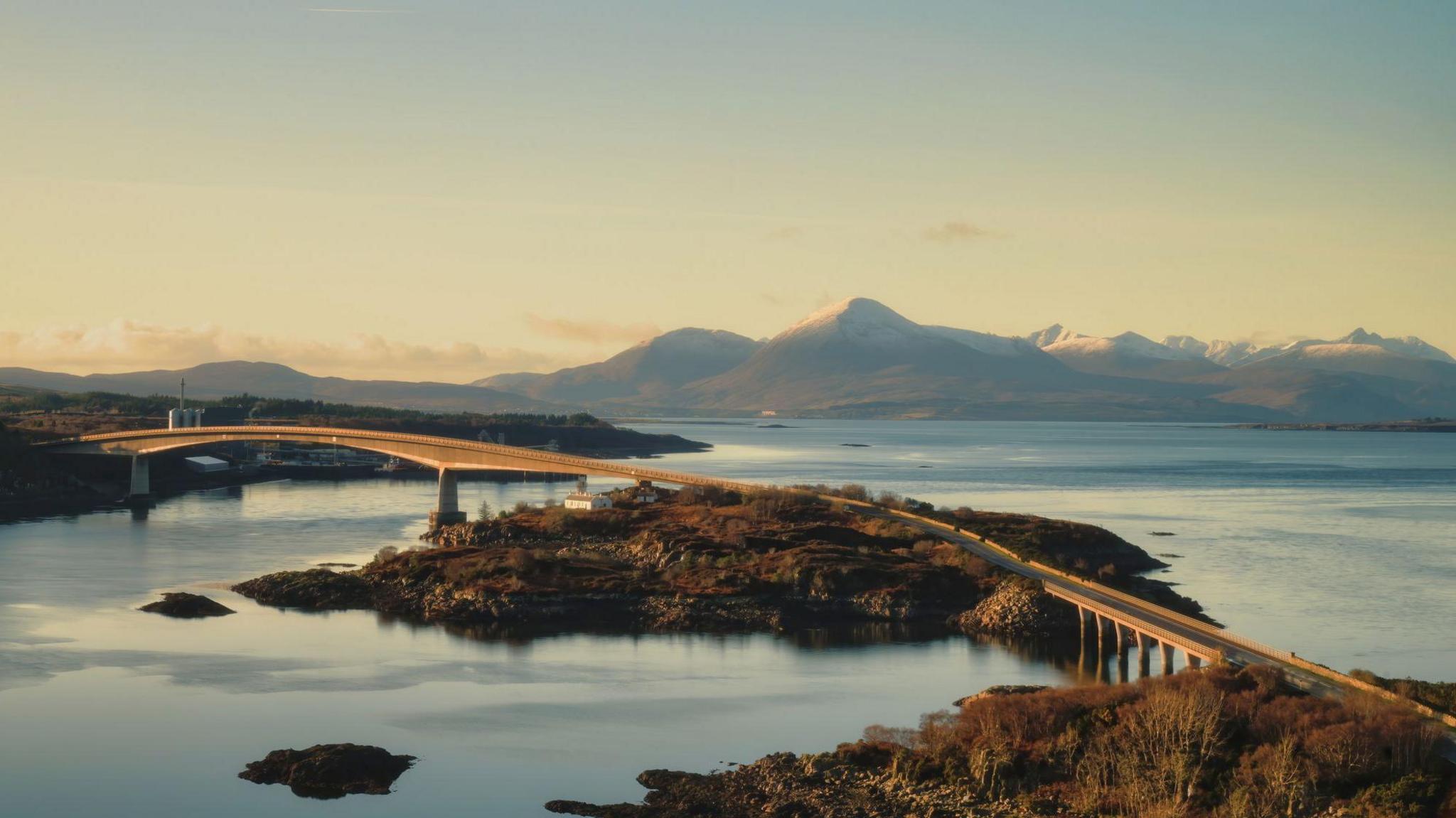 a scenic landscape of a blue sky and blue water with a bridge crossing between.