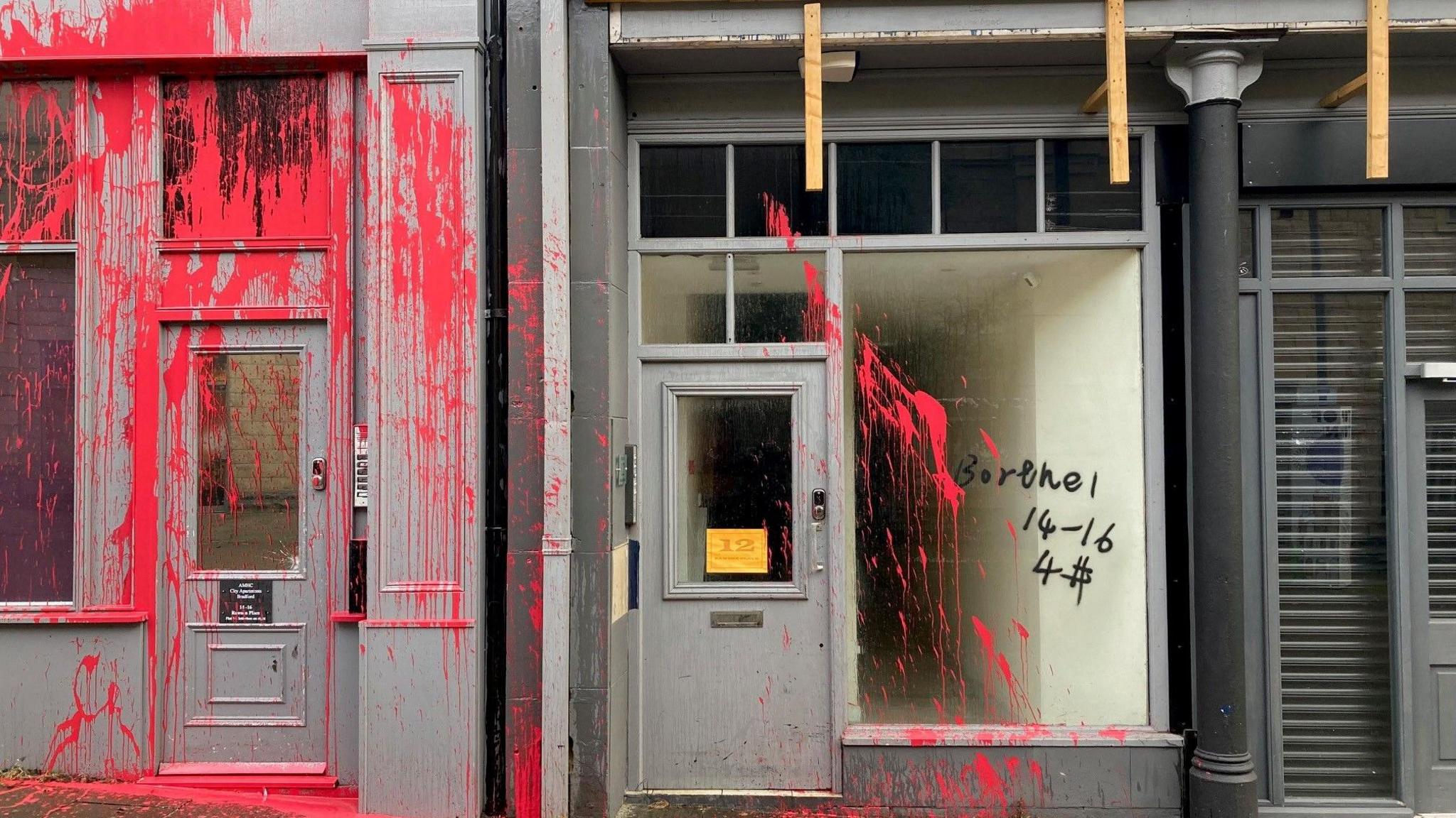 Red paint sprayed across two door ways which are entrances to apartments above ground floor retail units