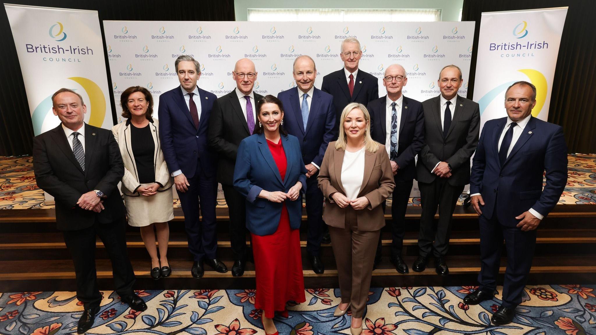 Political leaders from across Ireland, the UK and Crown Dependencies post for a photograph on a set of carpeted steps inside a building during the British-Irish Council summit. Hoardings are behind them with the British-Irish Council logo on.