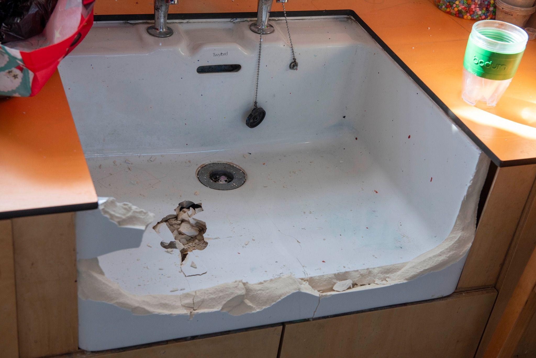 A white sink in an orange sideboard but the front piece of the sink has been smashed away. The bottom of the sink is also smashed.