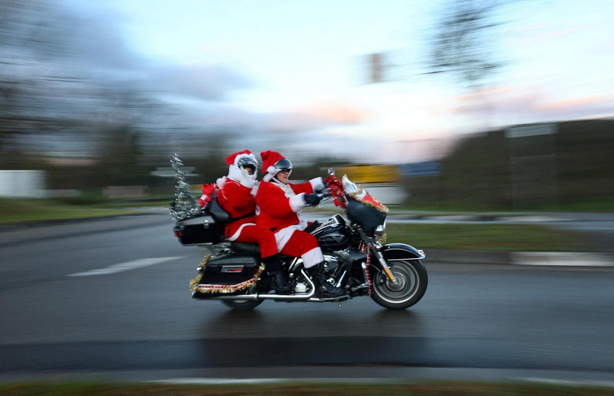 Two people dressed as Father Christmas on the back of a motorbike