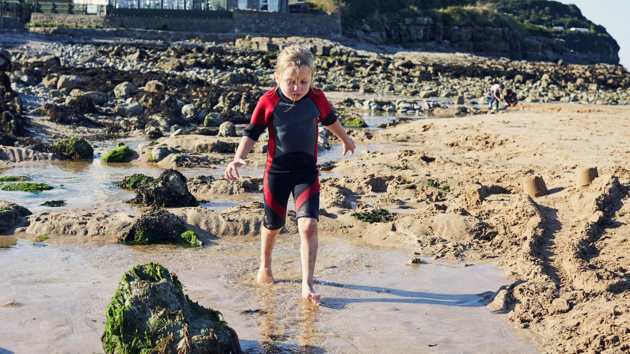 Child walking through water along beach.