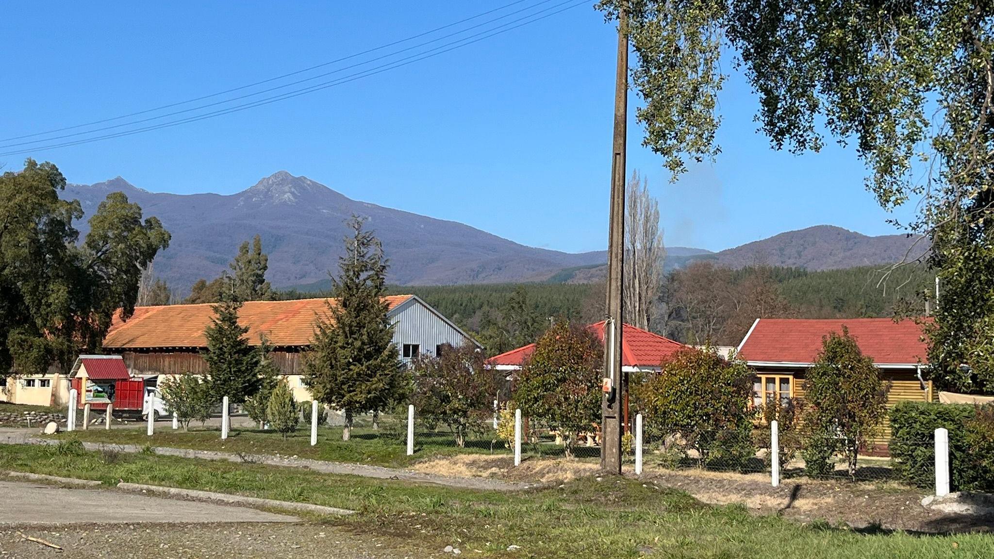 Behind white fence posts, three buildings with red roofs can be seen. One of them is made of wood, while another one is a larger barn-like structure. 