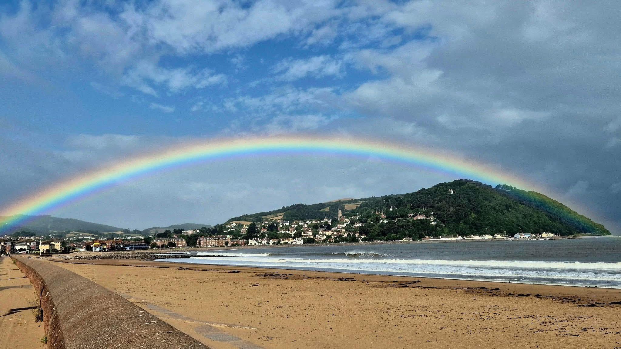 Partly cloudy sky with rainbow stretching over land and sea at a coastal town 