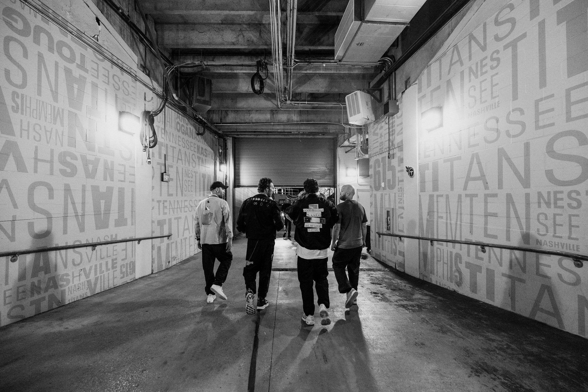 In a black and white photo, Coldplay walk down a tunnel in Nashville, with their backs to the camera