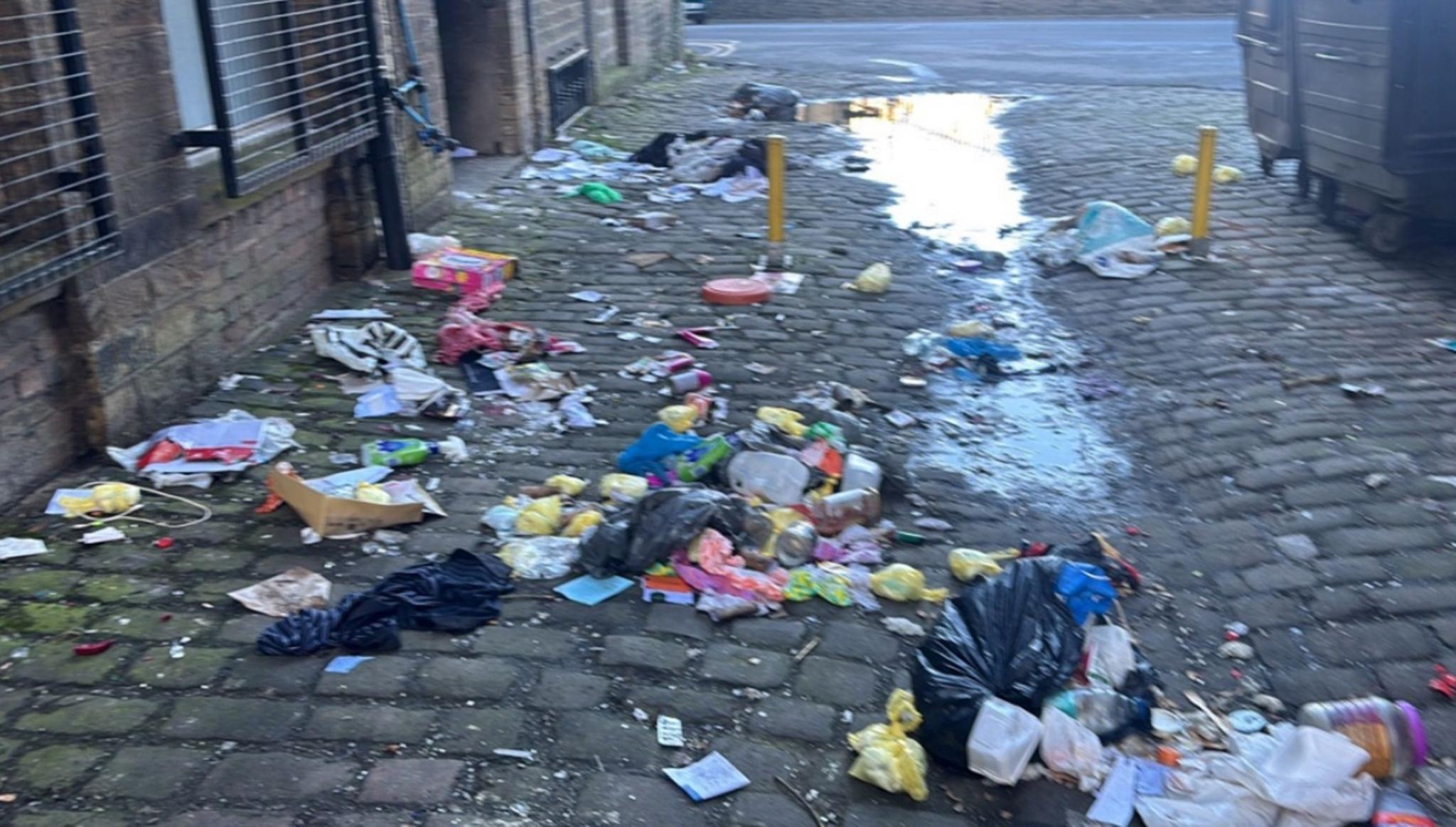 A cobbled passageway in Bradford which has been strewn with dumped litter which has spilled out from black bags