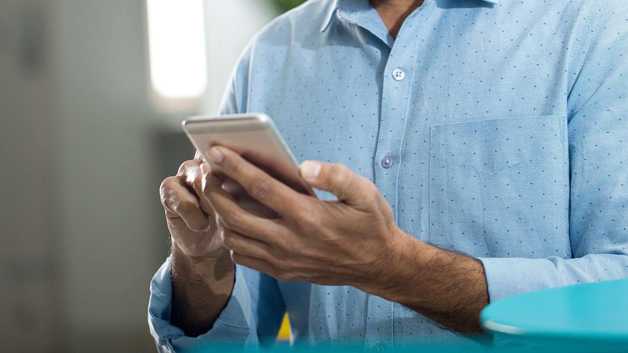 A man holds a phone in his hands while wearing a blue shirt