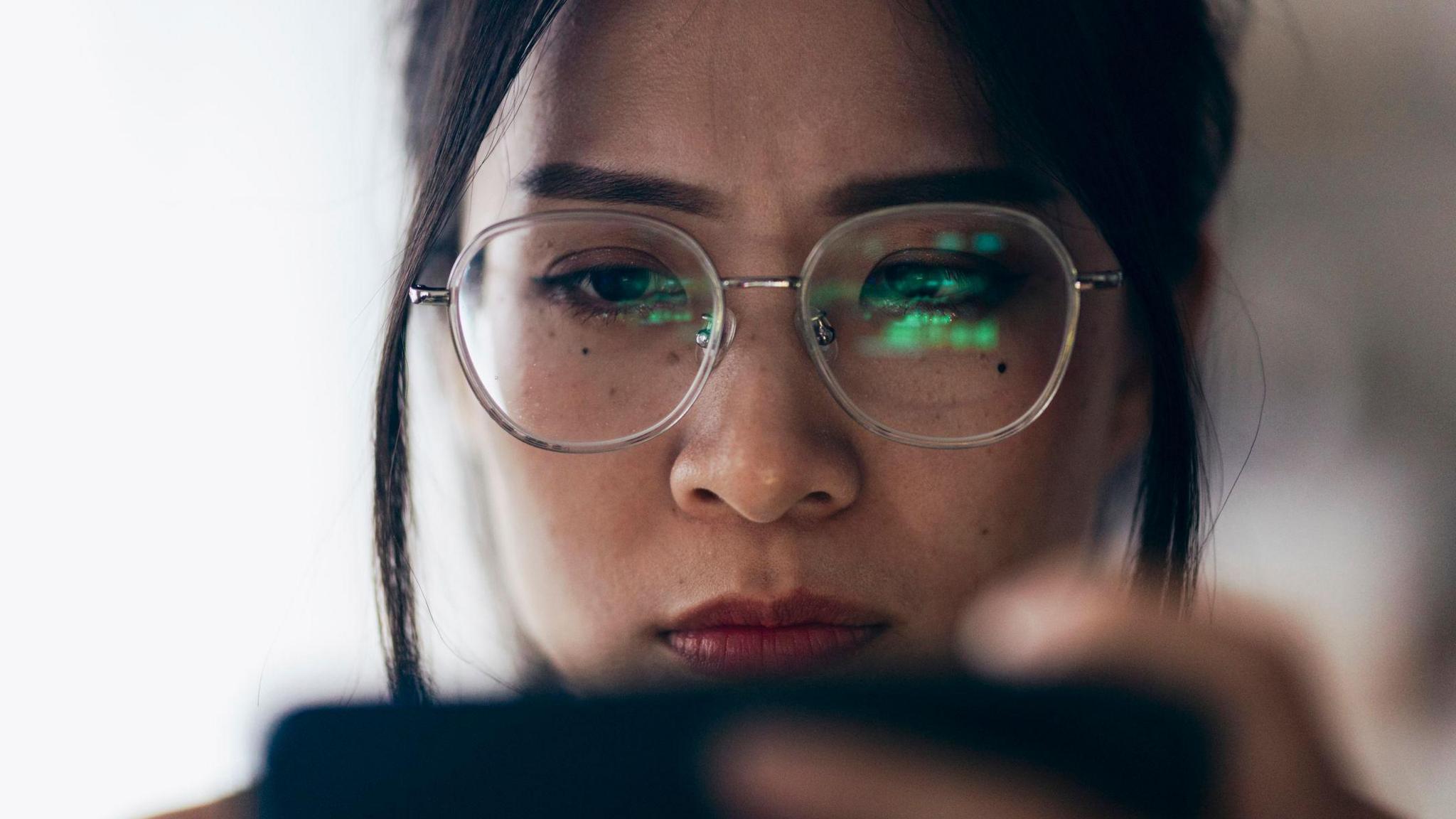 A woman using a phone, with the screen reflected in her glasses
