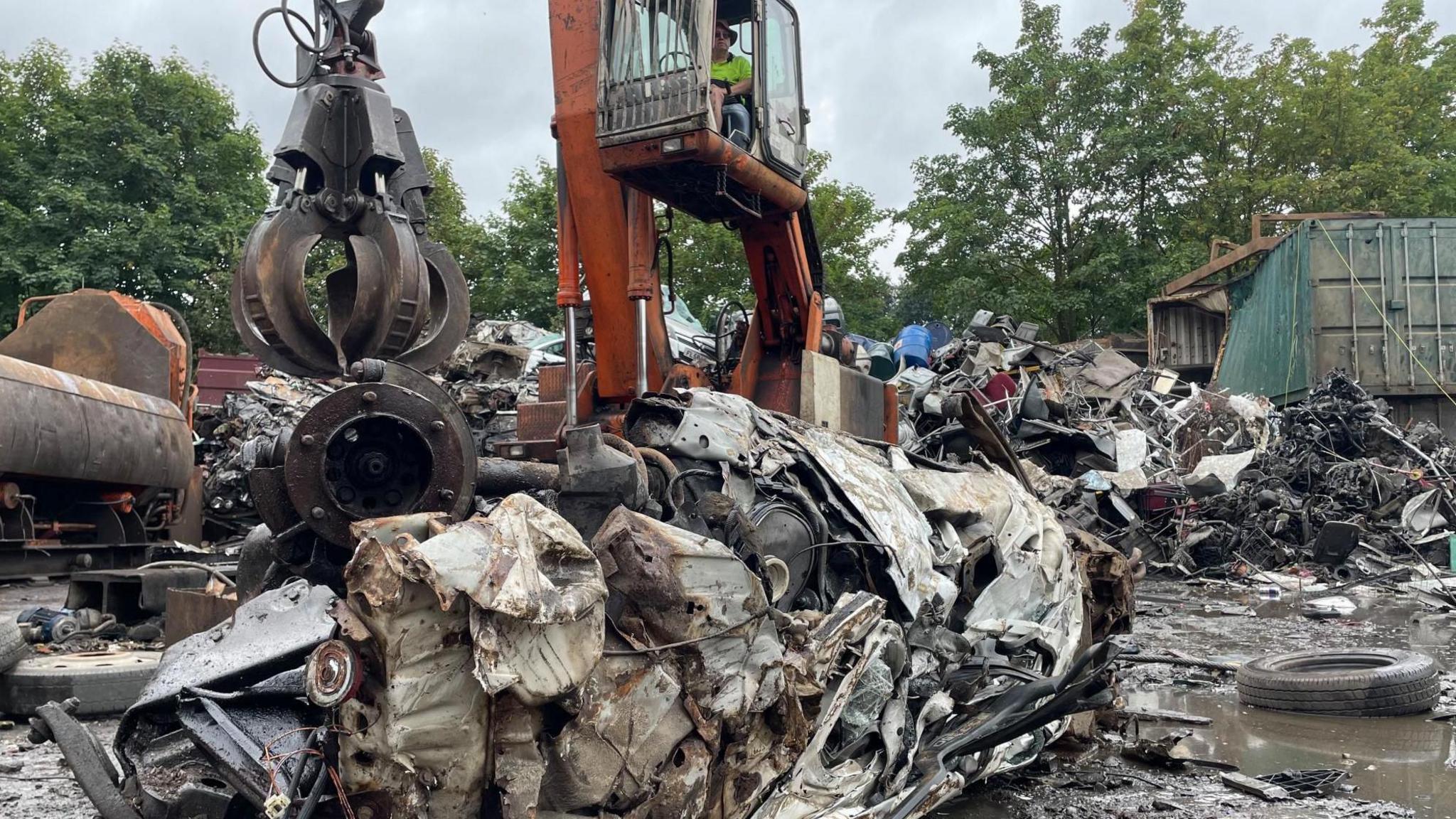 A man operating a crane looks down at a crushed mound of metal