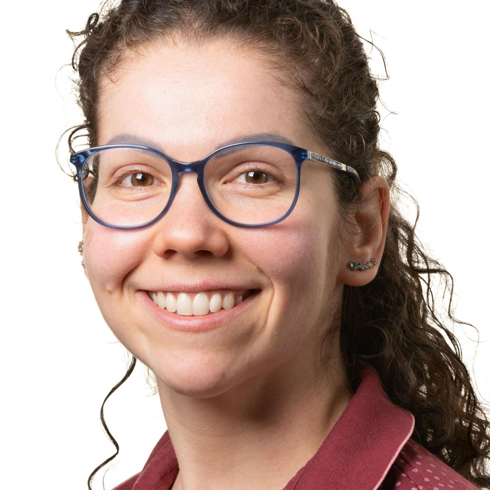 Renata Garbellini Duft smiling stood against a white background. She is wearing a red shirt and has blue glasses.