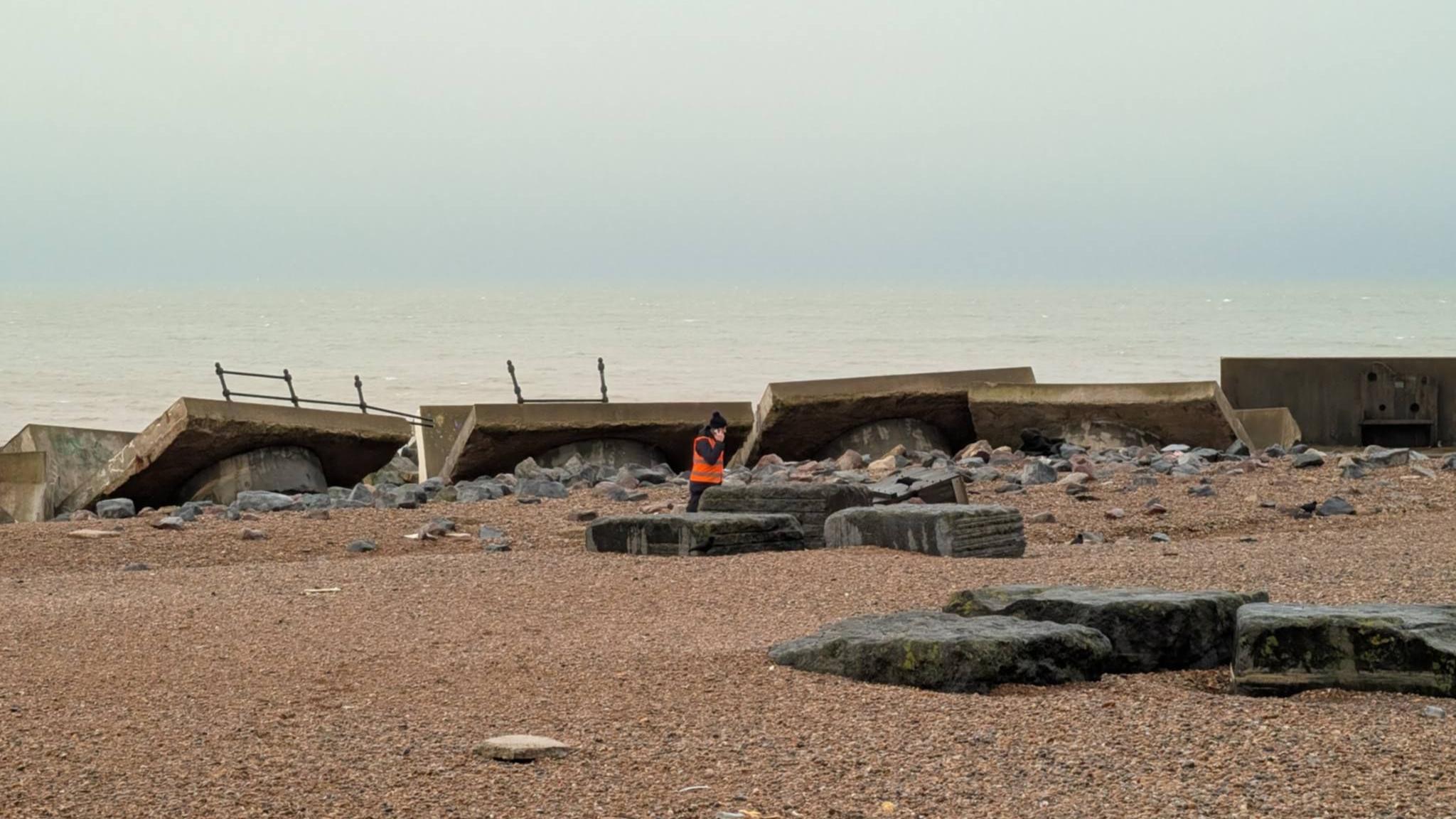 Picture shows collapsed sea wall and a man in a high vis assessing the scene.