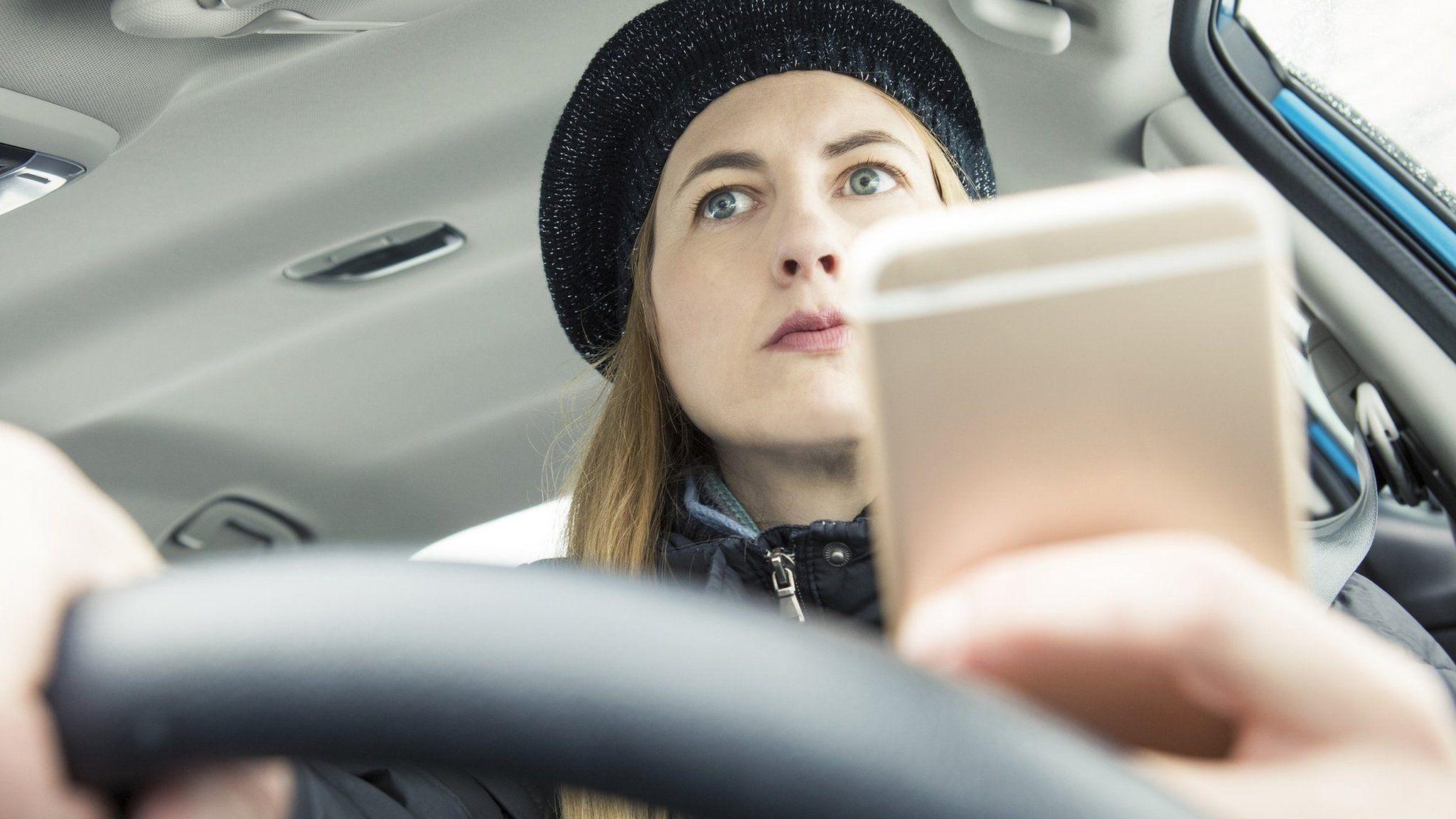 Woman with long hair wearing black hat uses phone in lorry cab