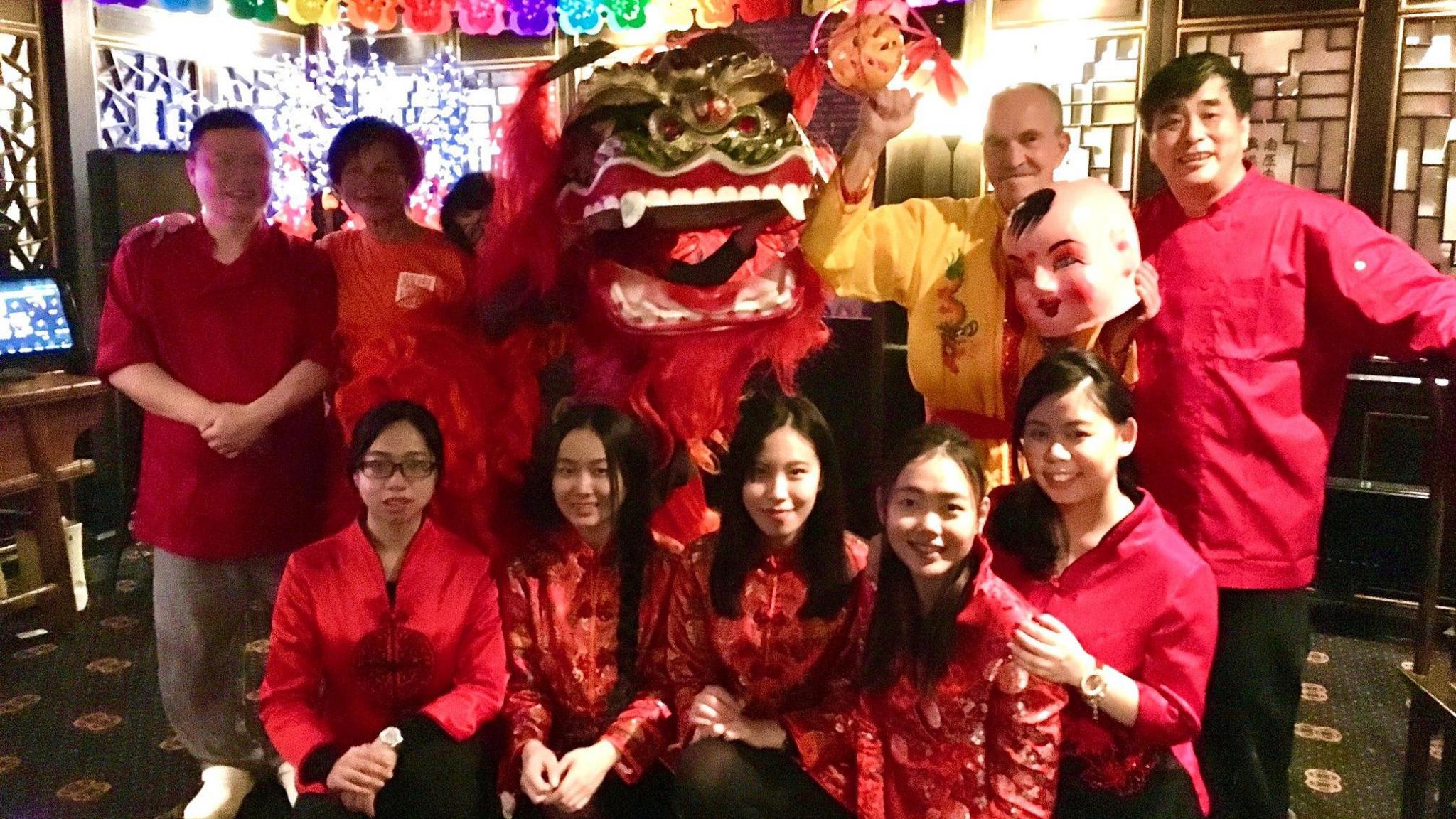 A group of staff at Chinese restaurant Wongs in Bristol pose together for a group shot, all wearing red uniforms of a satin-type material. Behind them is a large dragon created to celebrate the Lunar New Year