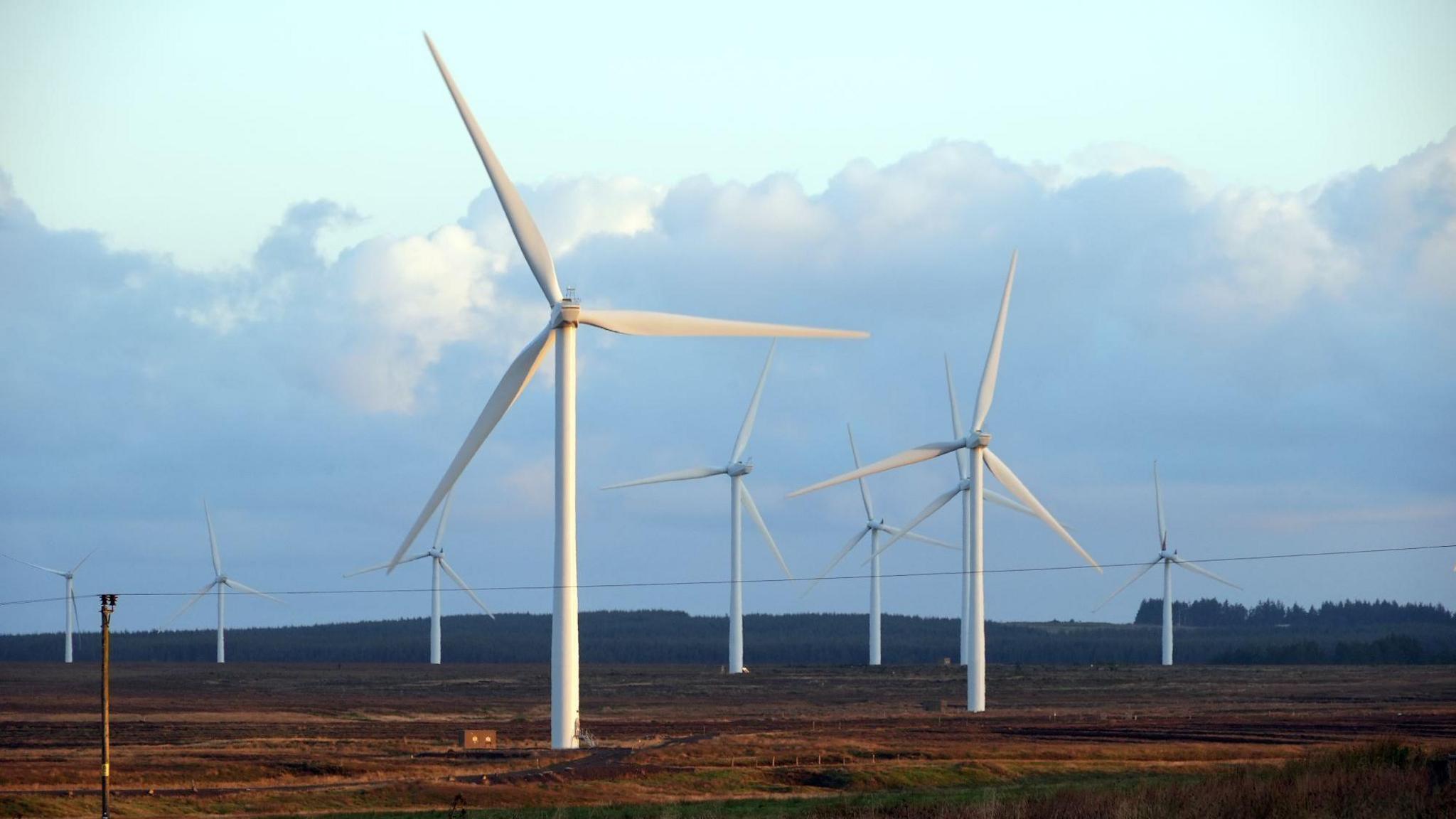 Landscape image of a wind farm in the Scottish Highlands showing two in the foregroung and seven in the far distance